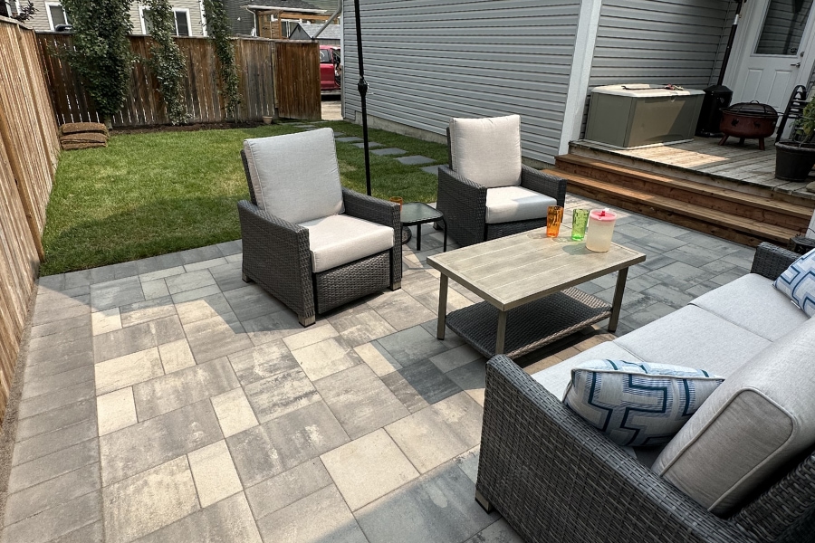 Backyard large format interlocking paver patio with wicker outdoor furniture and a fresh lawn, landscape construction in Calgary by Western Elements Landscaping