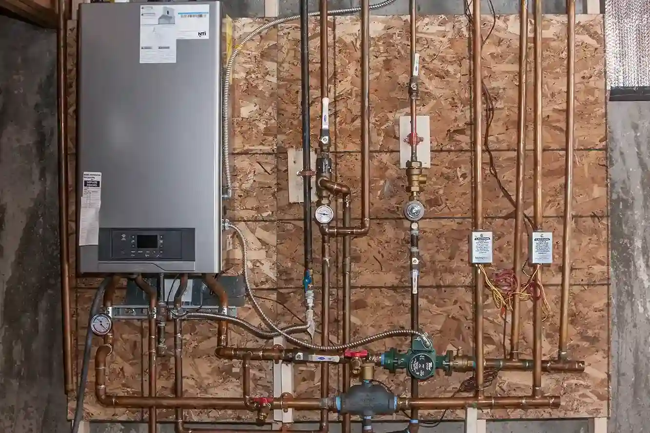 A full shot of a complex plumbing setup featuring a silver tankless water heater, with an intricate network of copper pipes and gauges mounted on a wooden wall.