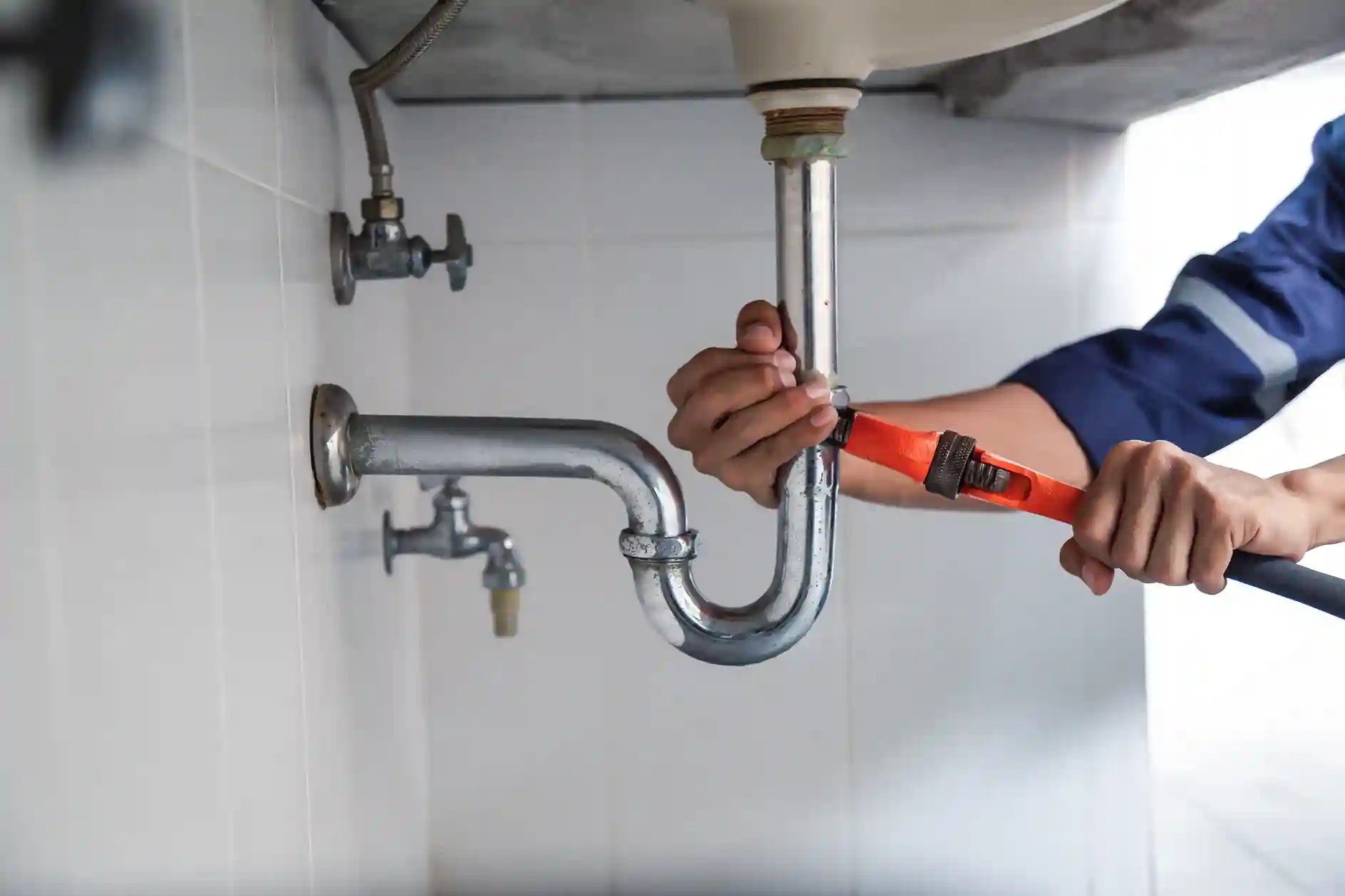 Plumber using an orange wrench to perform maintenance on a chrome sink P-trap.