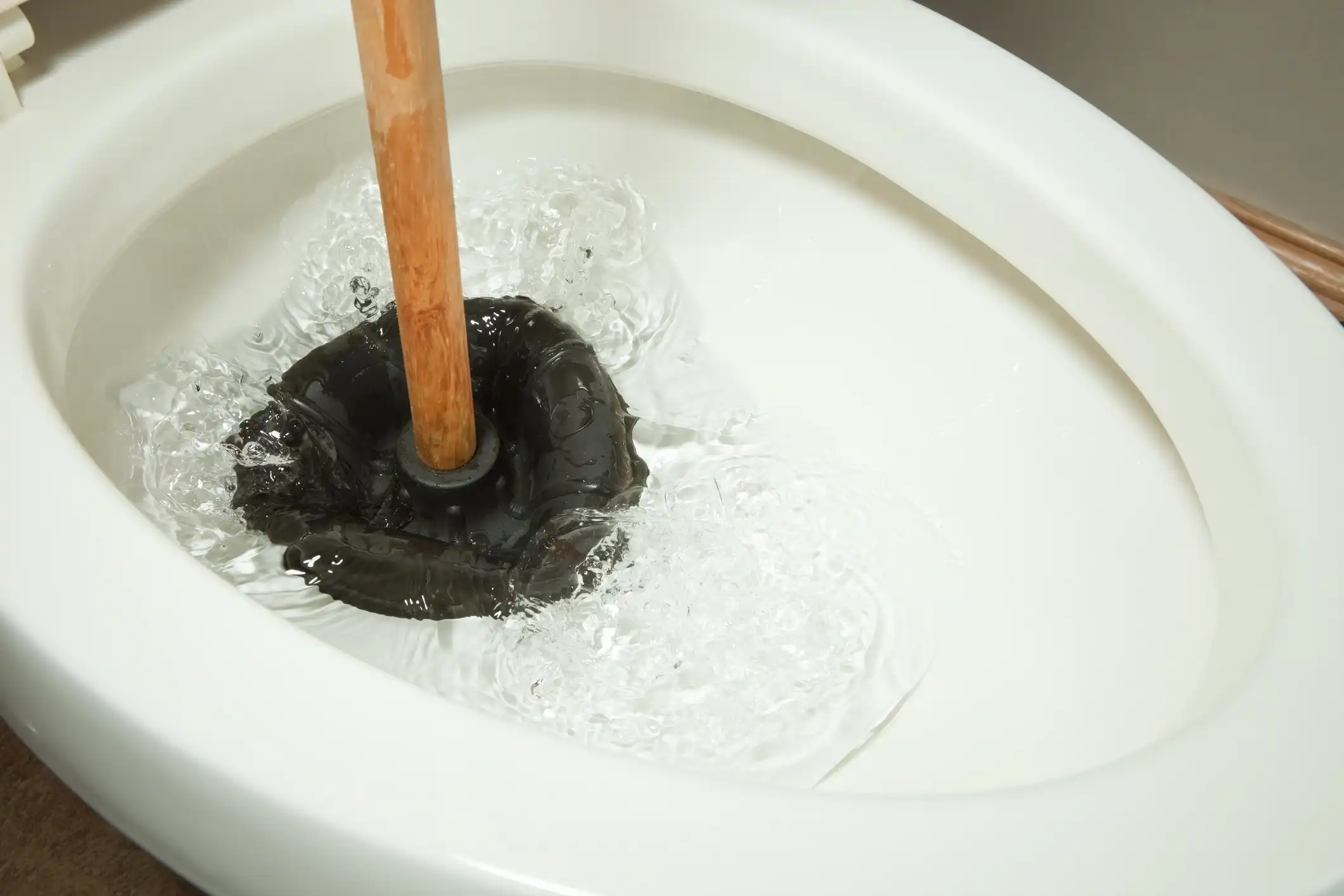 A plunger is submerged in a toilet bowl with water splashing around it.