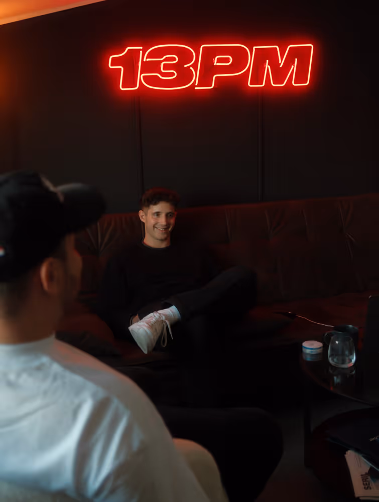 Toby Romeo auf einer Couch unter einem roten 13PM LED Schild