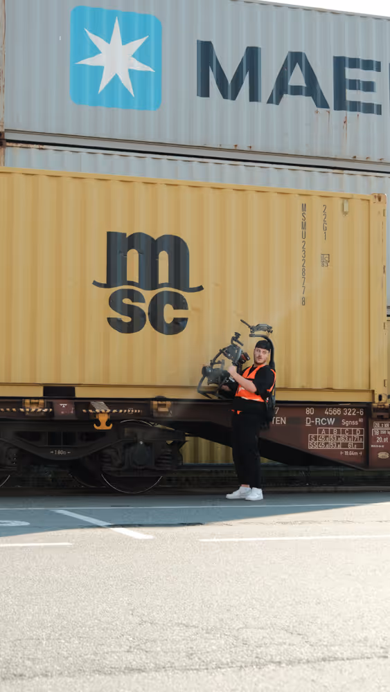Ein Mann mit einer Kamera vor einem Container und einer Warnweste