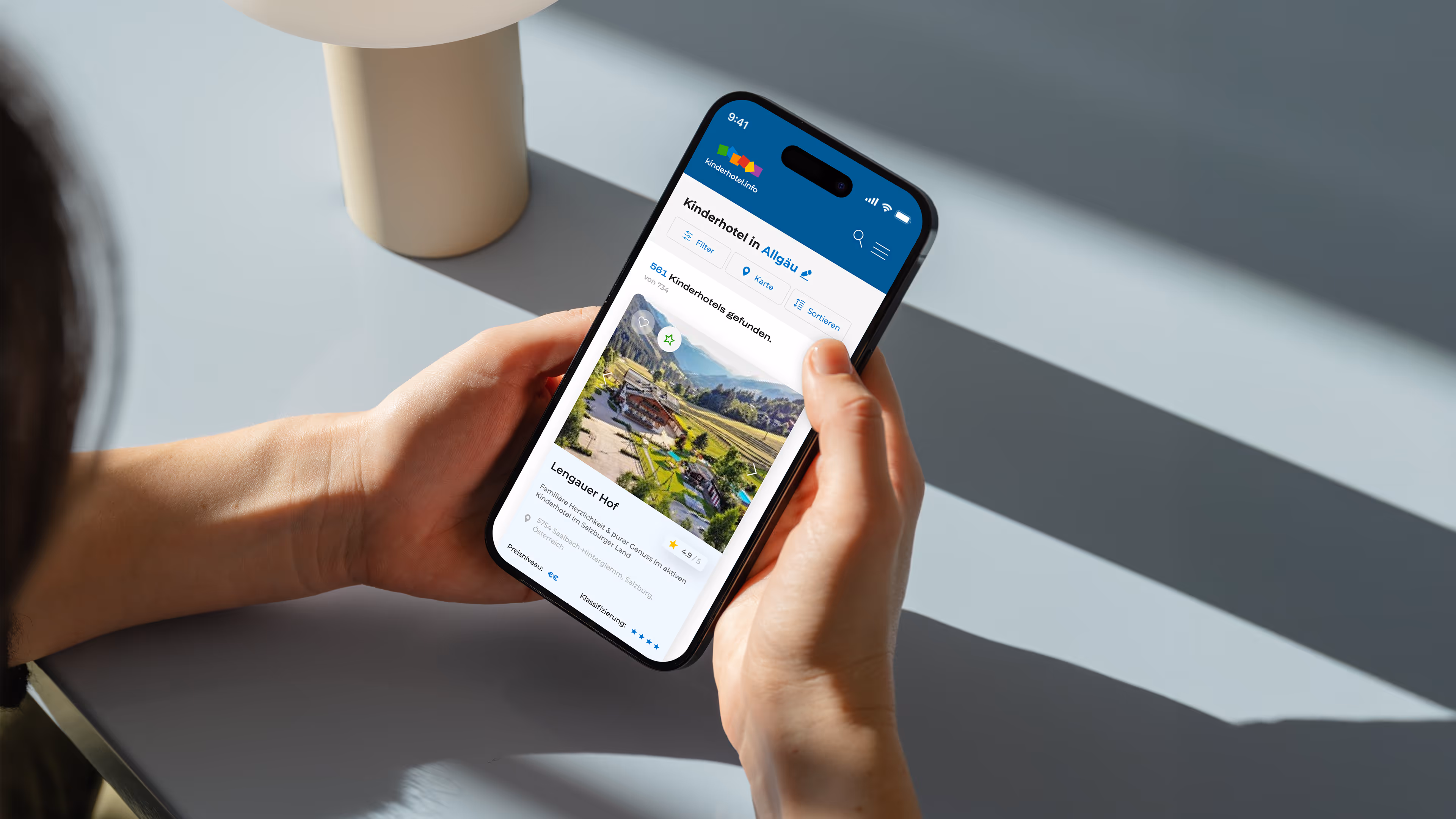Person hält ein Smartphone, das eine Webseite mit einem Kinderhotel namens Lengauer Hof in Allgäu zeigt.