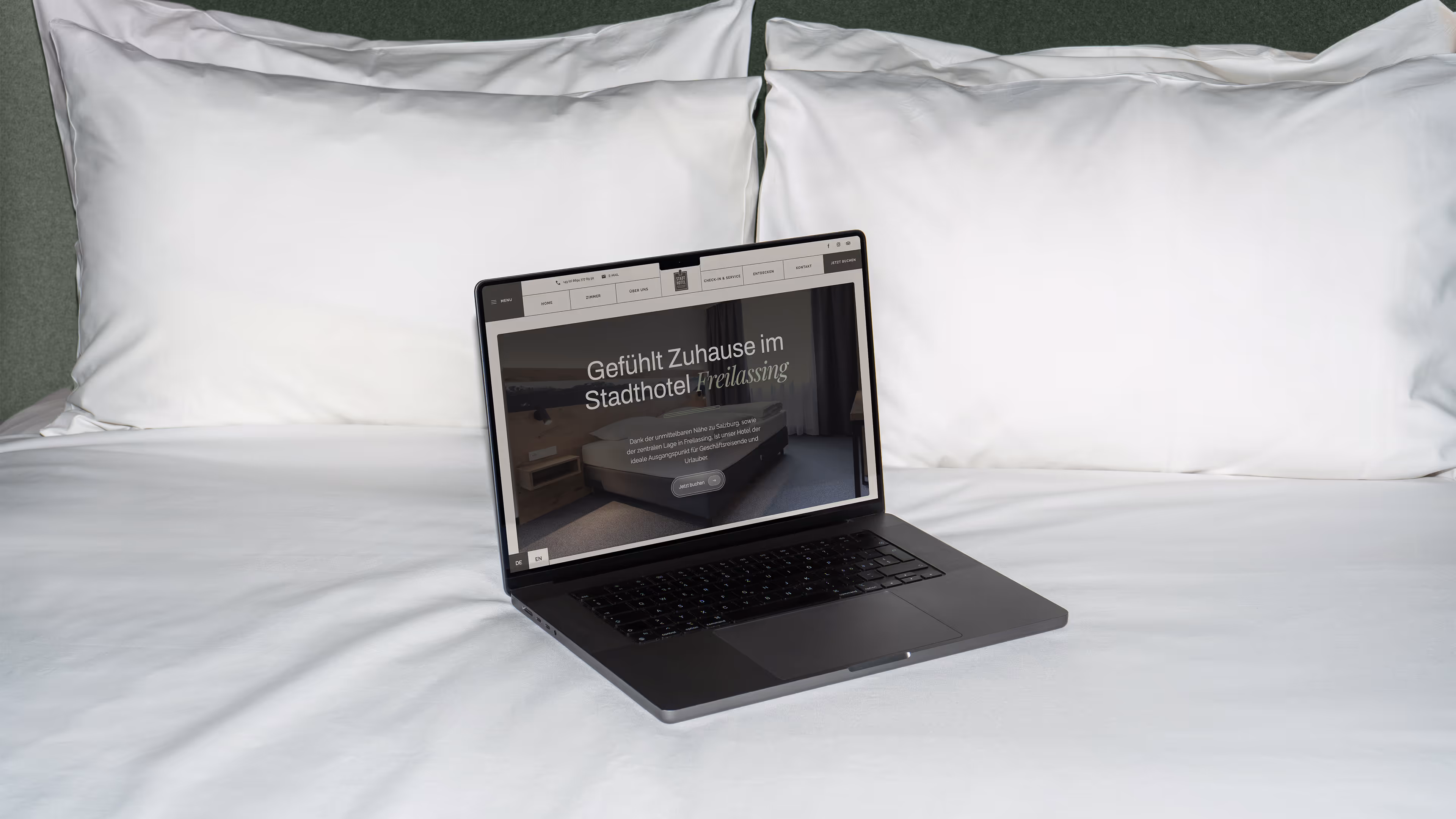 Offener Laptop auf einem weißen Hotelbett zeigt die Webseite des Stadthotels Freilassing.