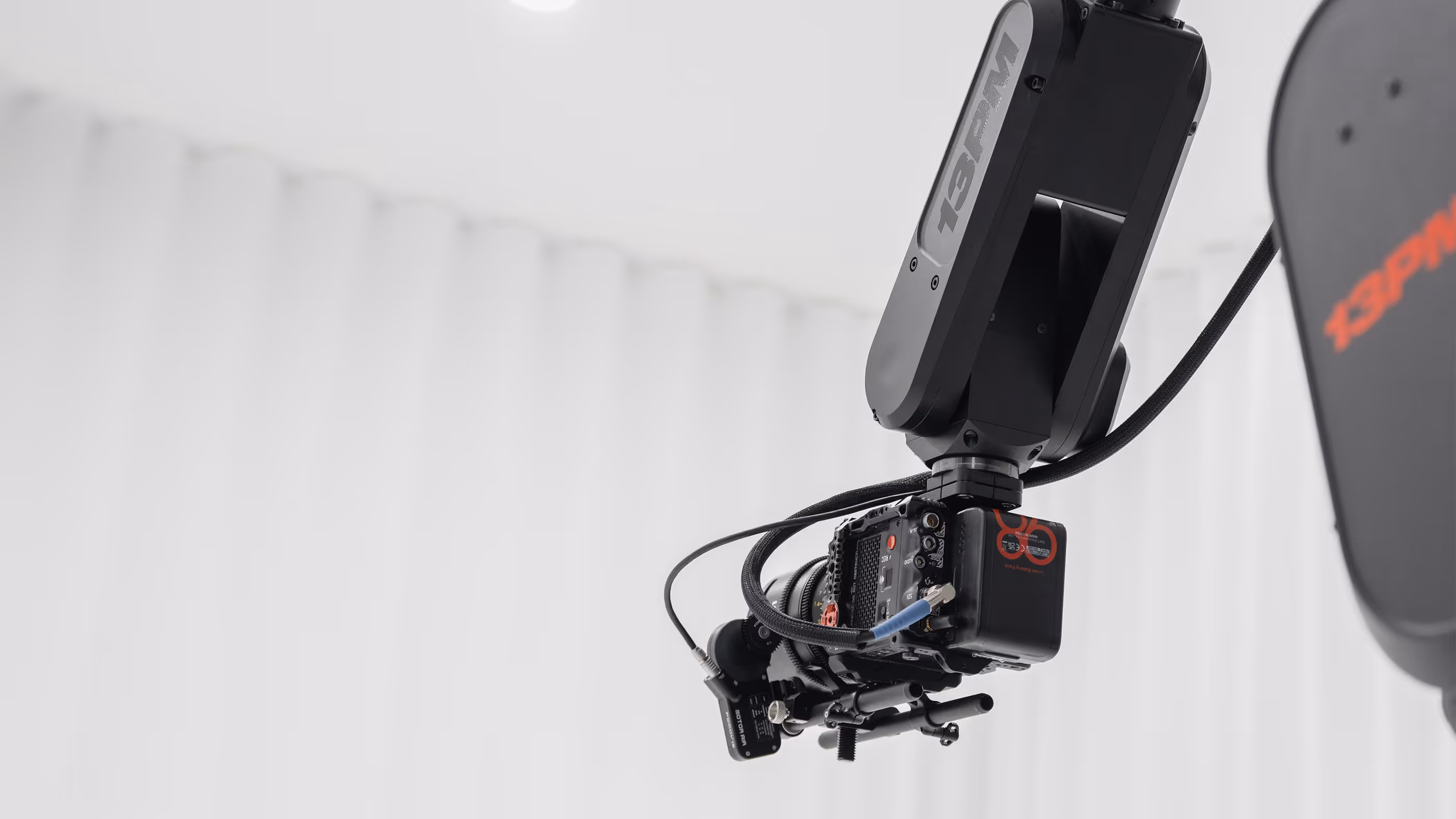 Professionelle Filmkamera montiert an einem schwarzen 13PM Roboterarm vor weißem Hintergrund.