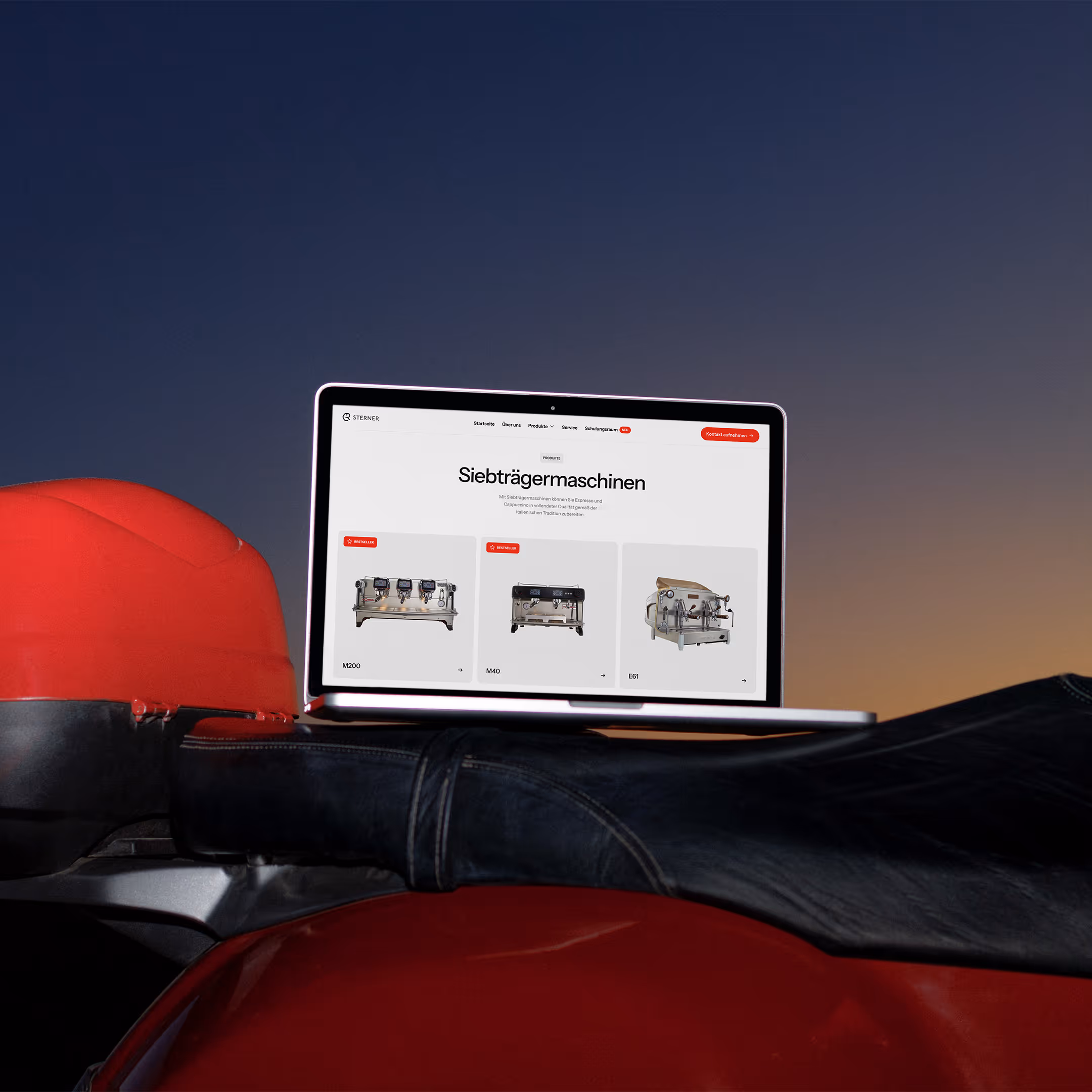 Laptop zeigt eine Webseite mit Siebträgermaschinen vor einem Abendhimmel, platziert auf dem Sitz eines roten Motorrads.