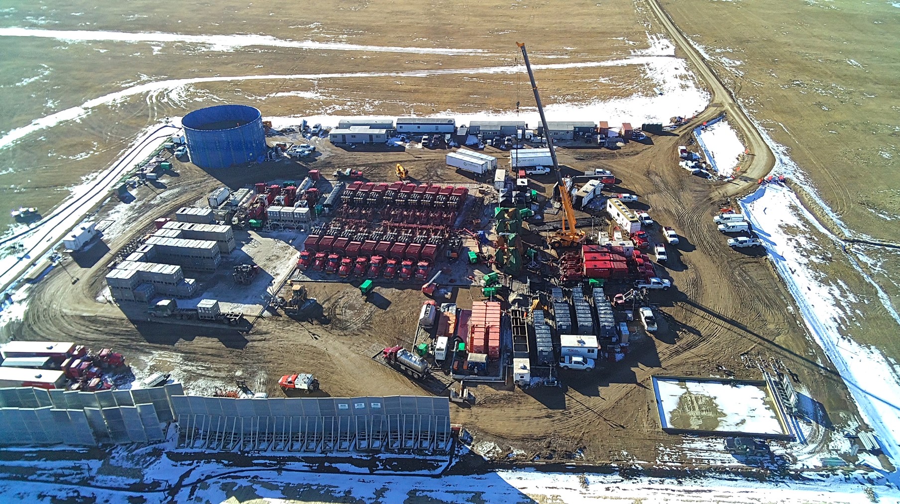 Aerial view of a large industrial frac spread site with machinery, trucks, containers, and dirt roads.