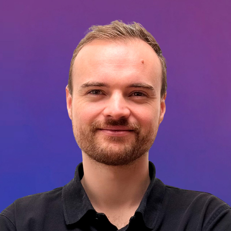 Portrait of Mr. Engels with beard and short hair in blue and pink light against a monochrome background.