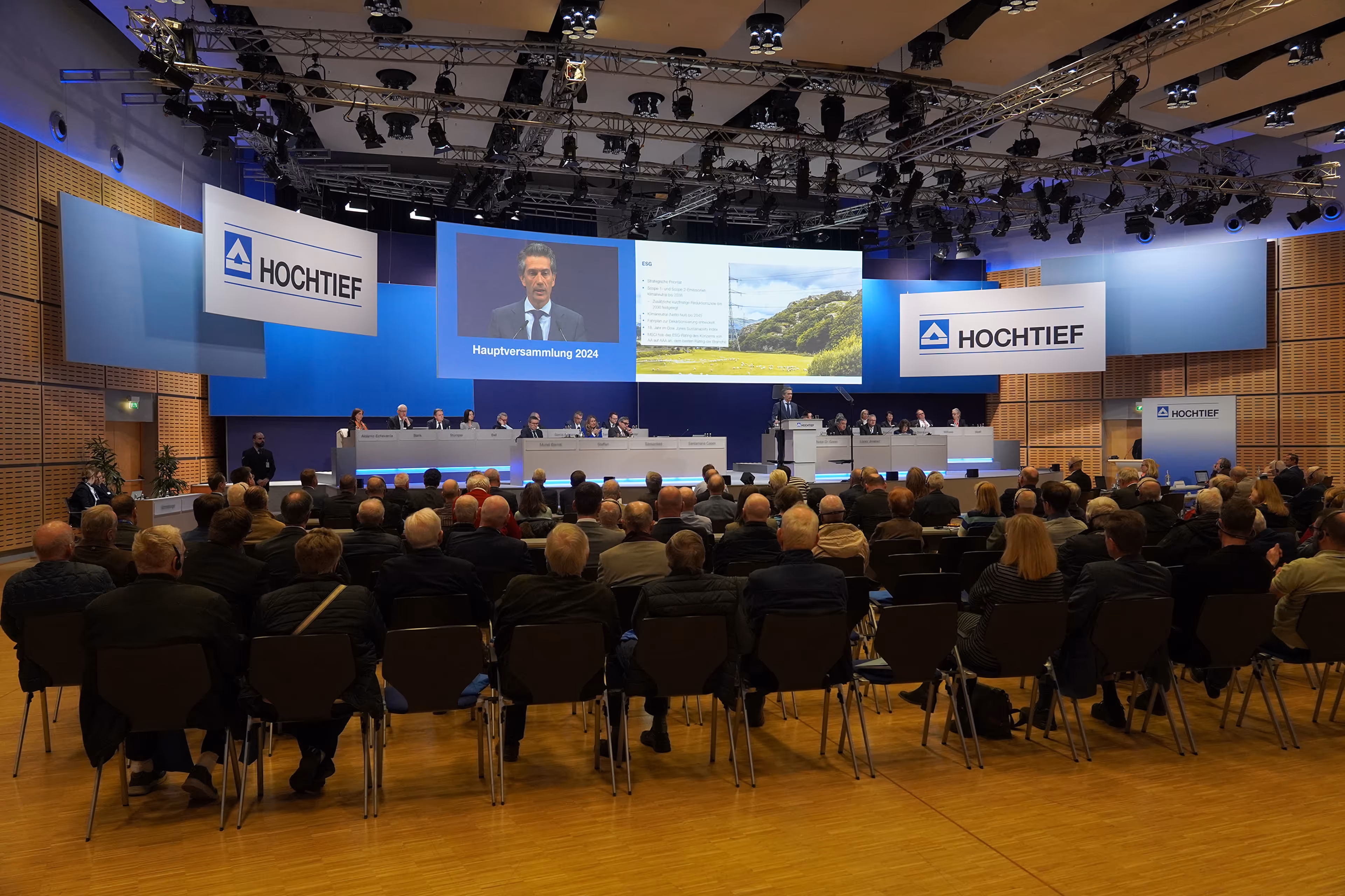Hauptversammlung 2024 von HOCHTIEF mit Publikum, Podium und Präsentation auf großen Bildschirmen in modernem Konferenzsaal.