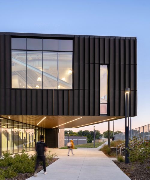 A modern high school is pictured. A walkway runs underneath a cantilevered room. 
