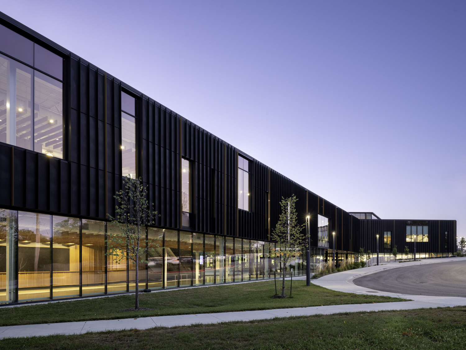 Exterior of high school building with tall glass windows ans students walking outside.
