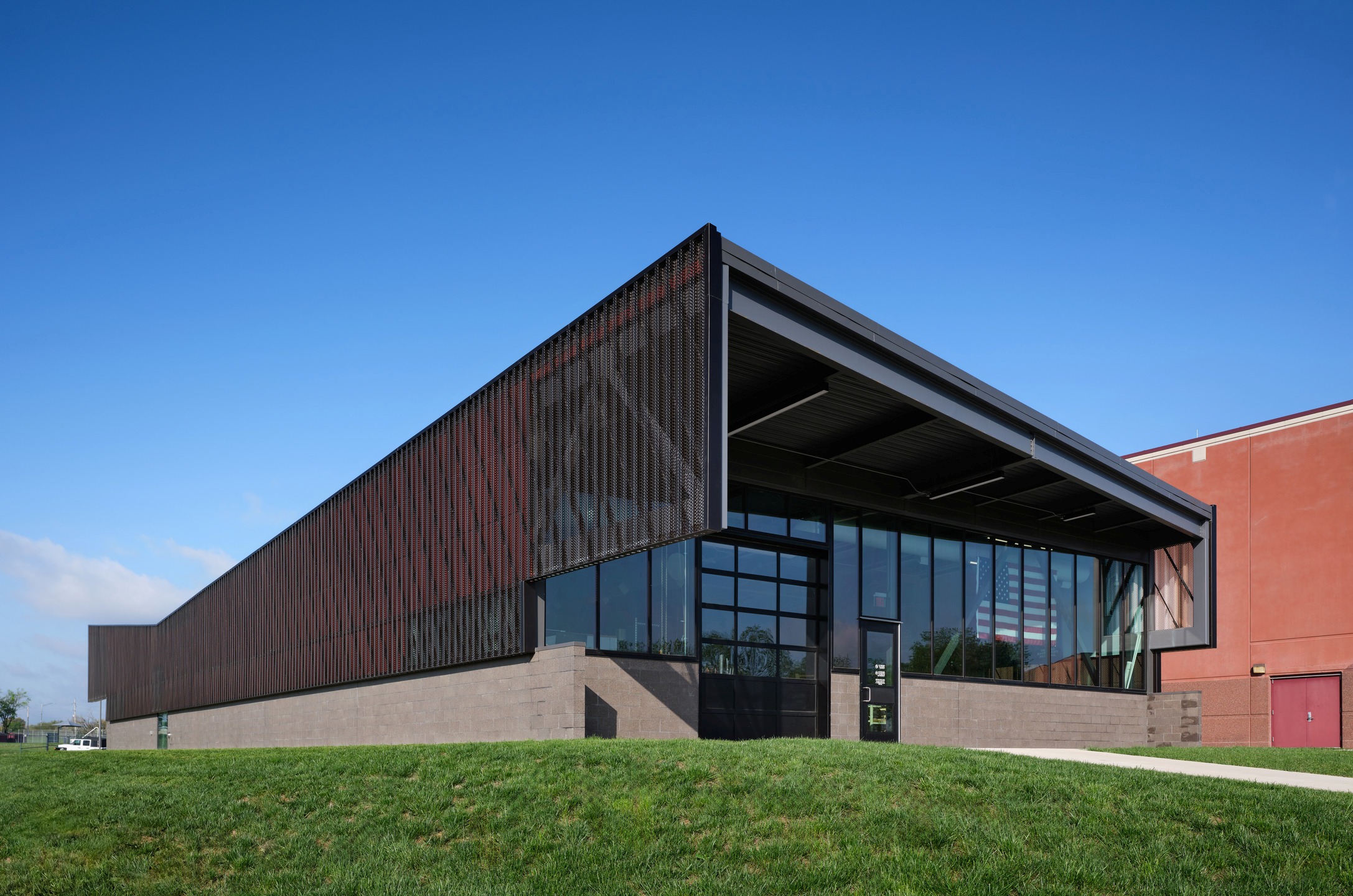 An aluminum scrim surrounds an angular stone and glass building. 