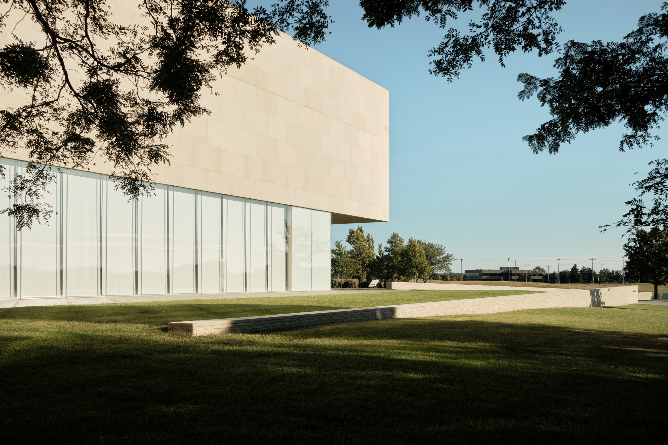 A limestone and glass building exterior contrasts with green lawn and blue sky. 