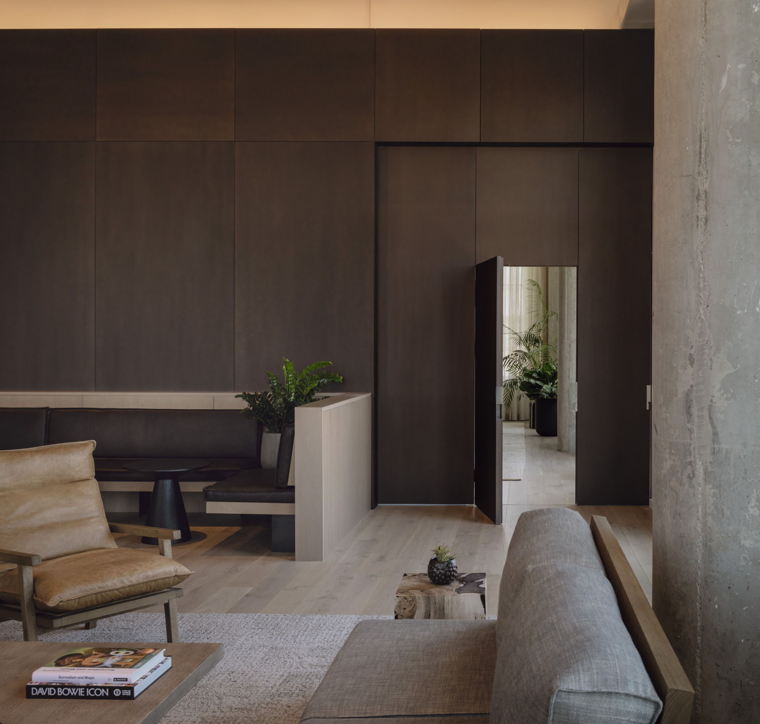Metal, concrete, and wood accents are softened with potted plants and sunlight from high windows. 