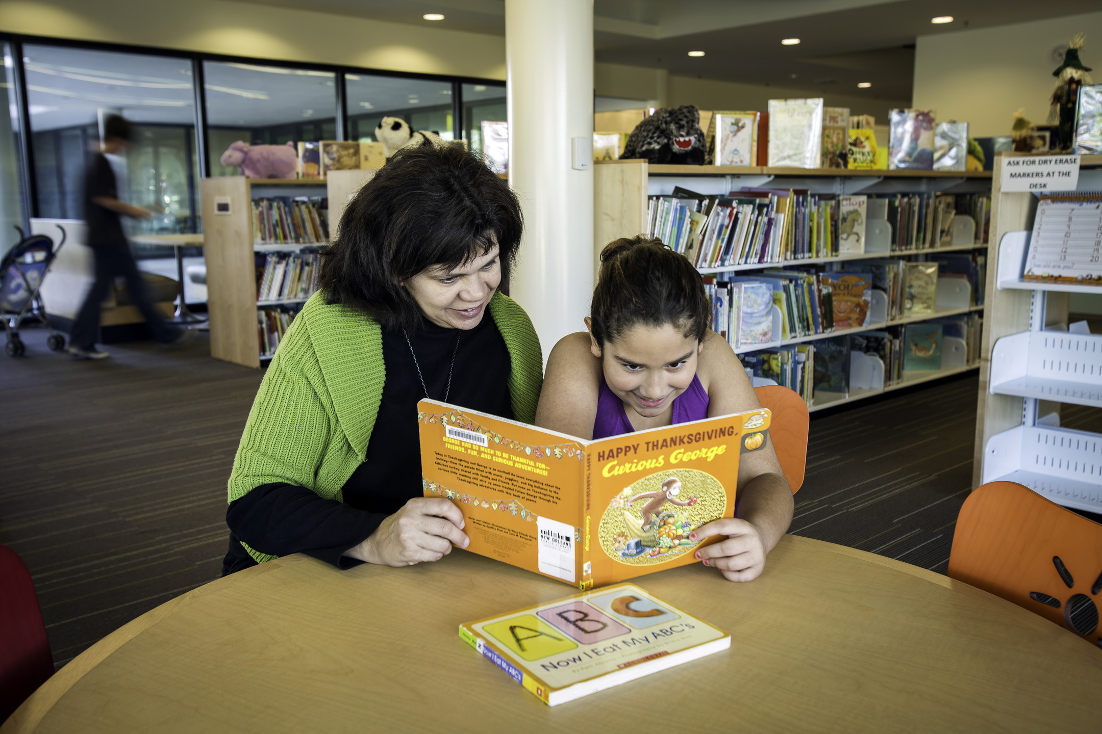 An adult and child read a book together in the children's area of the library.
