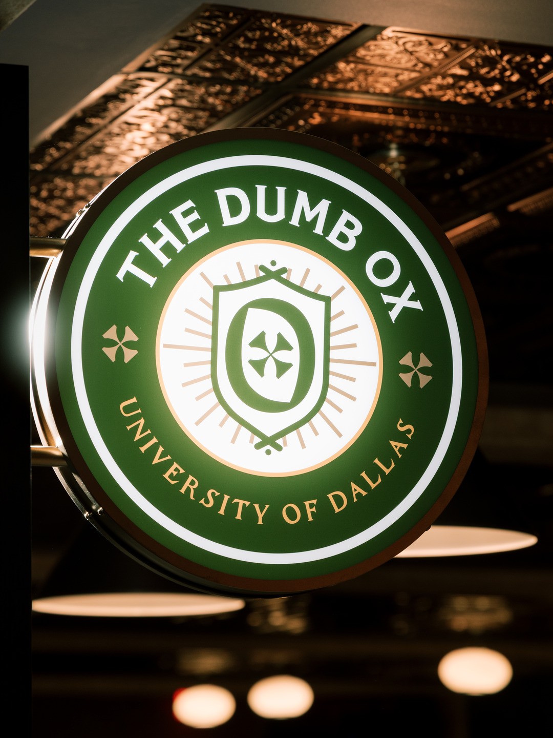 A backlit green, white, and tan sign adorned with the Dumb Ox logo is a bright beacon in the low-light pub. 
