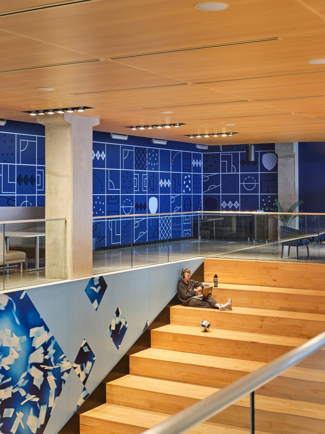 A team member works on the giant staircase connecting the upper and lower levels. The upper wall is adorned with graphics mimicking shapes from a soccer pitch.