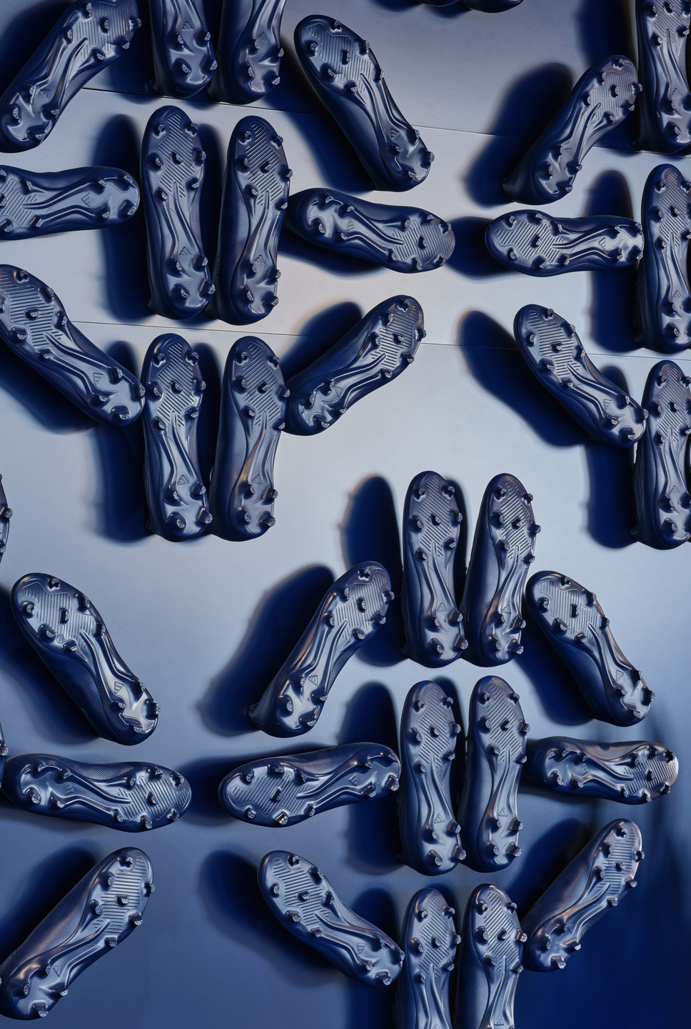 Two white chairs sit in front of a dark blue wall adorned with darker blue soccer cleats arranged in a pattern of diamonds. 