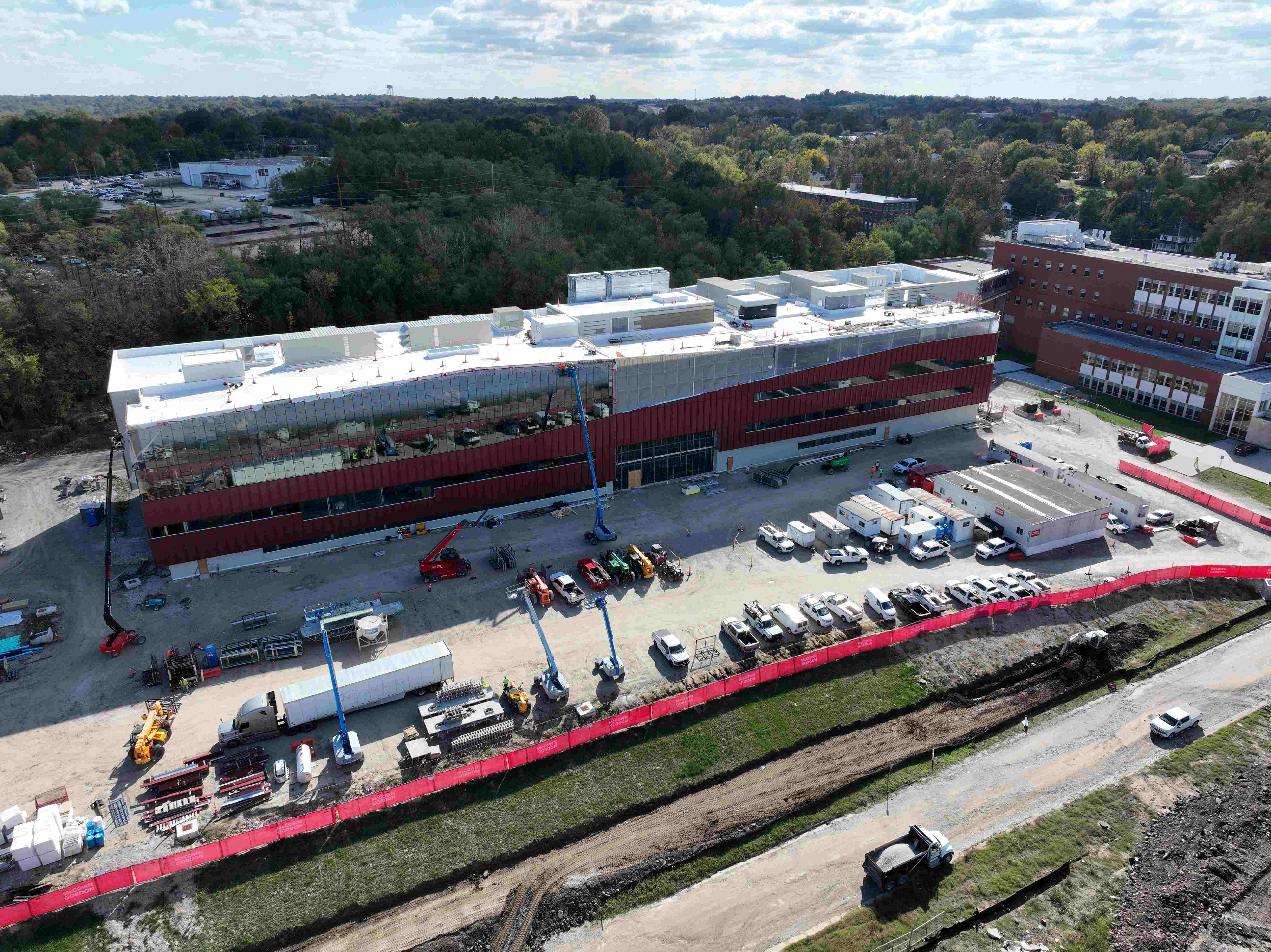 Glass sheeting and a burnt orange envelope enclose a rectangular laboratory building actively under construction..