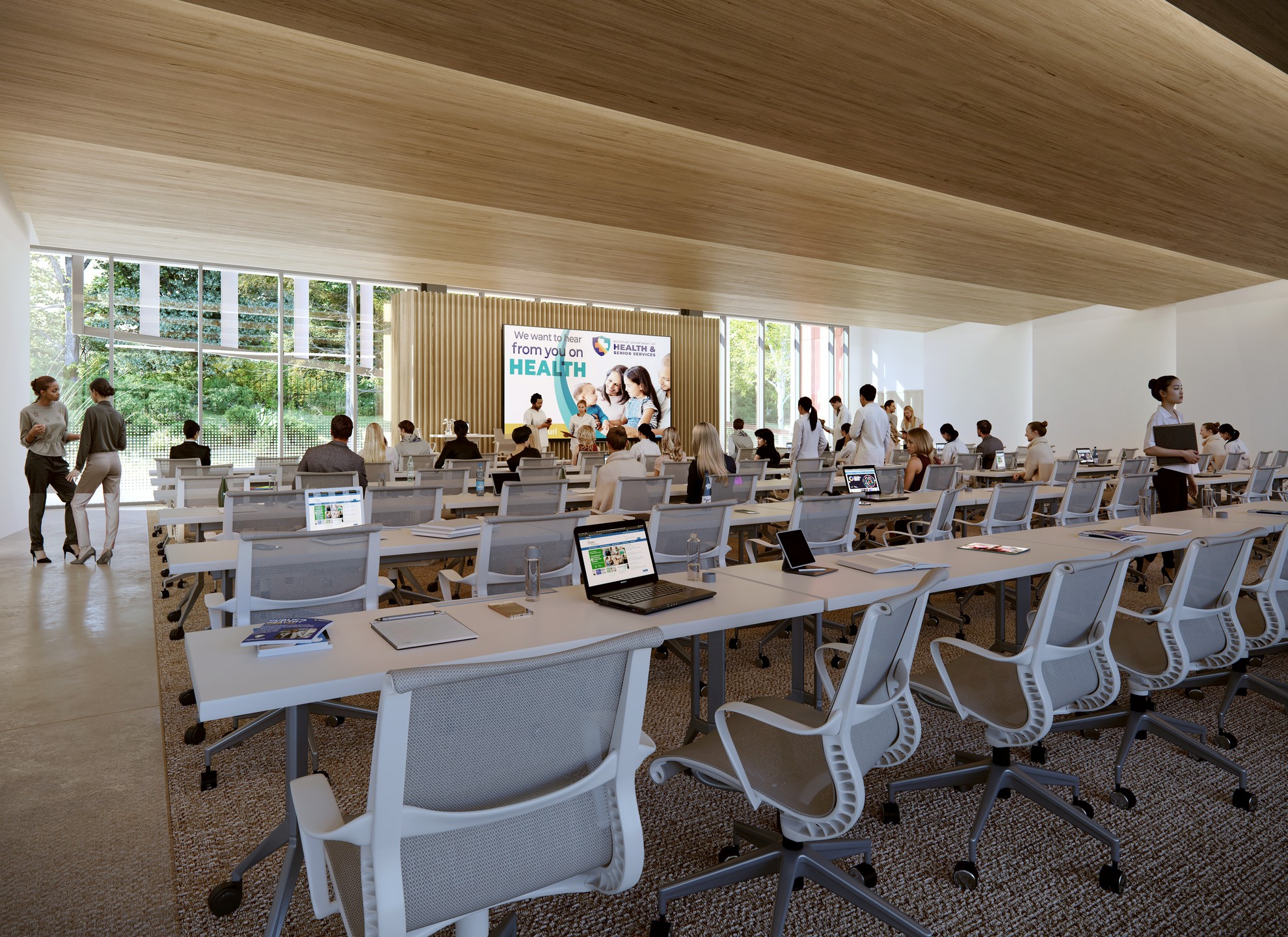 A rendering shows white desks and chairs lined up in a presentation space with a light wood ceiling. 