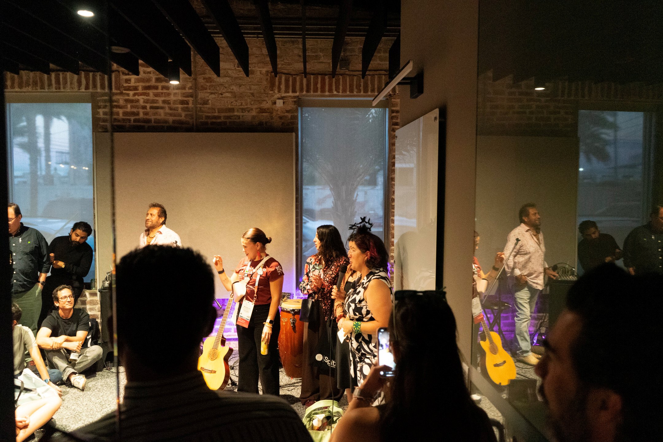 Musicians perform in front of an audience in an office space.