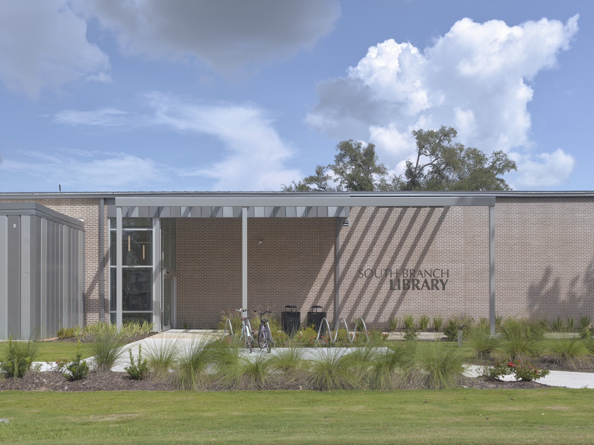 Clouds dot a pale blue sky over the South Branch Library's front facade, composed of brown brick and a steel awning.