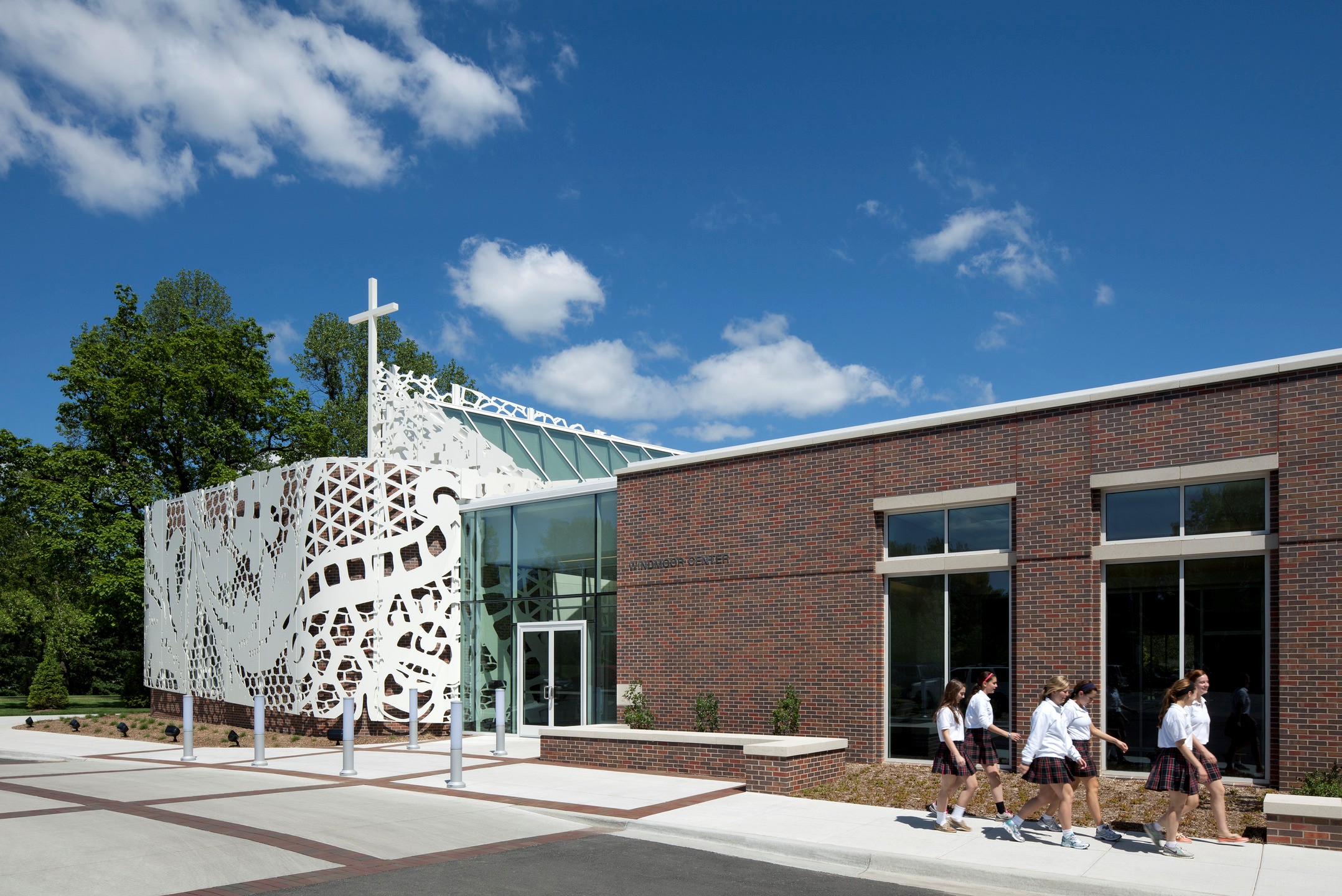 Uniformed students walk in front of a brick and glass building that features a white aluminum scrim cut to look like lace.
