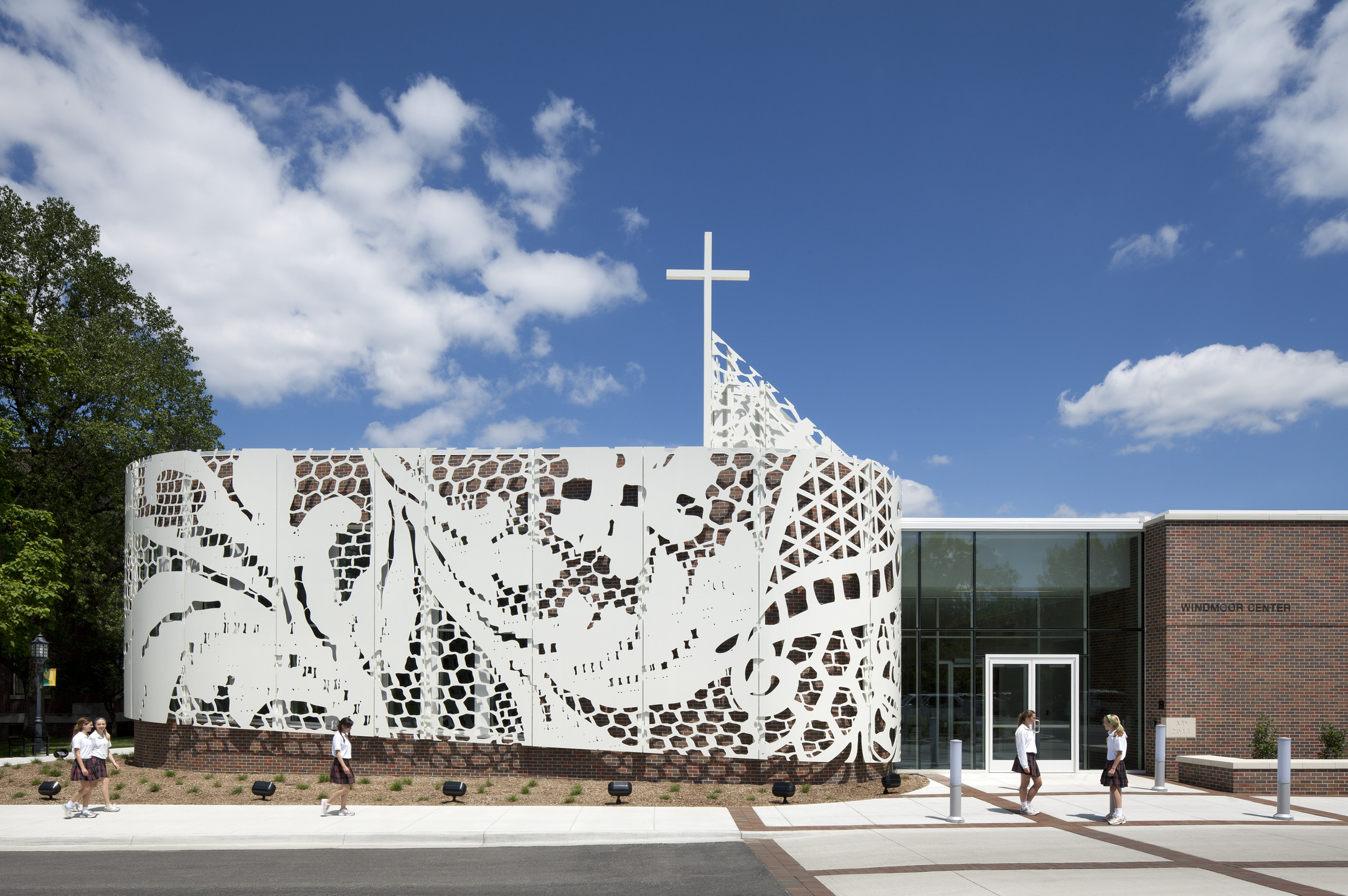 A brick and glass building features a white aluminum scrim cut to look like lace. 