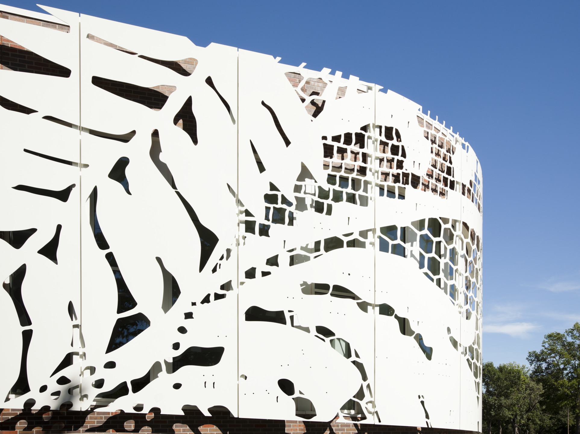 A brick and glass building features a white aluminum scrim cut to look like lace.