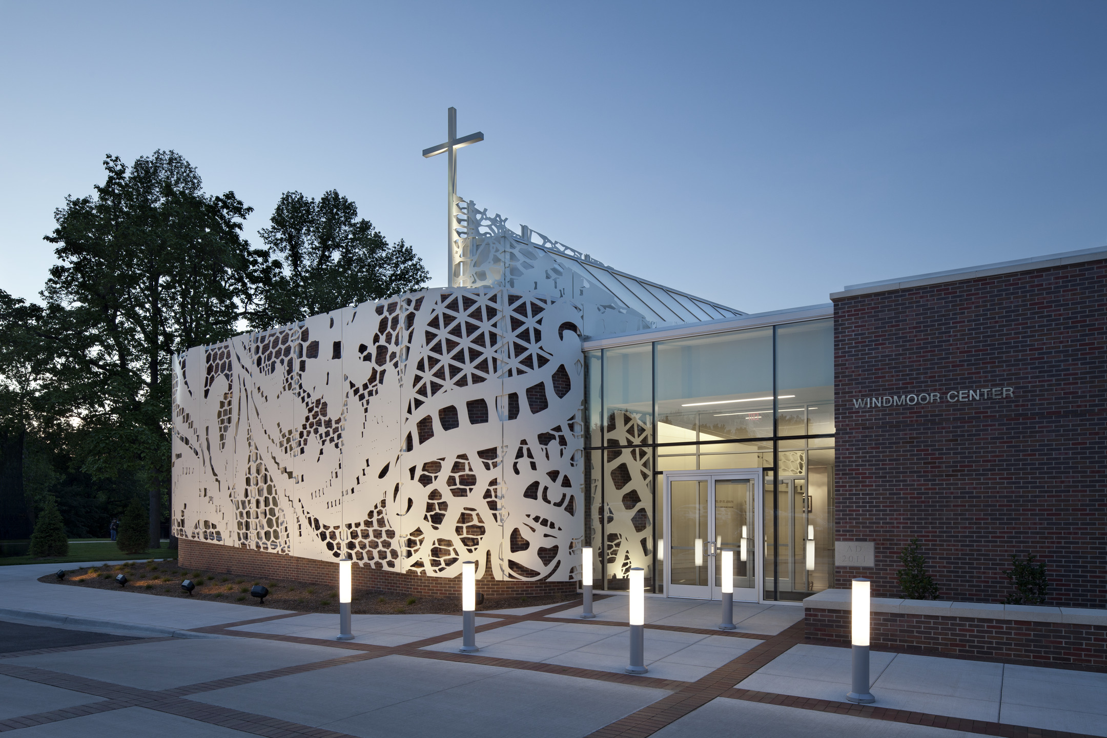 A brick and glass building features a white aluminum scrim cut to look like lace.