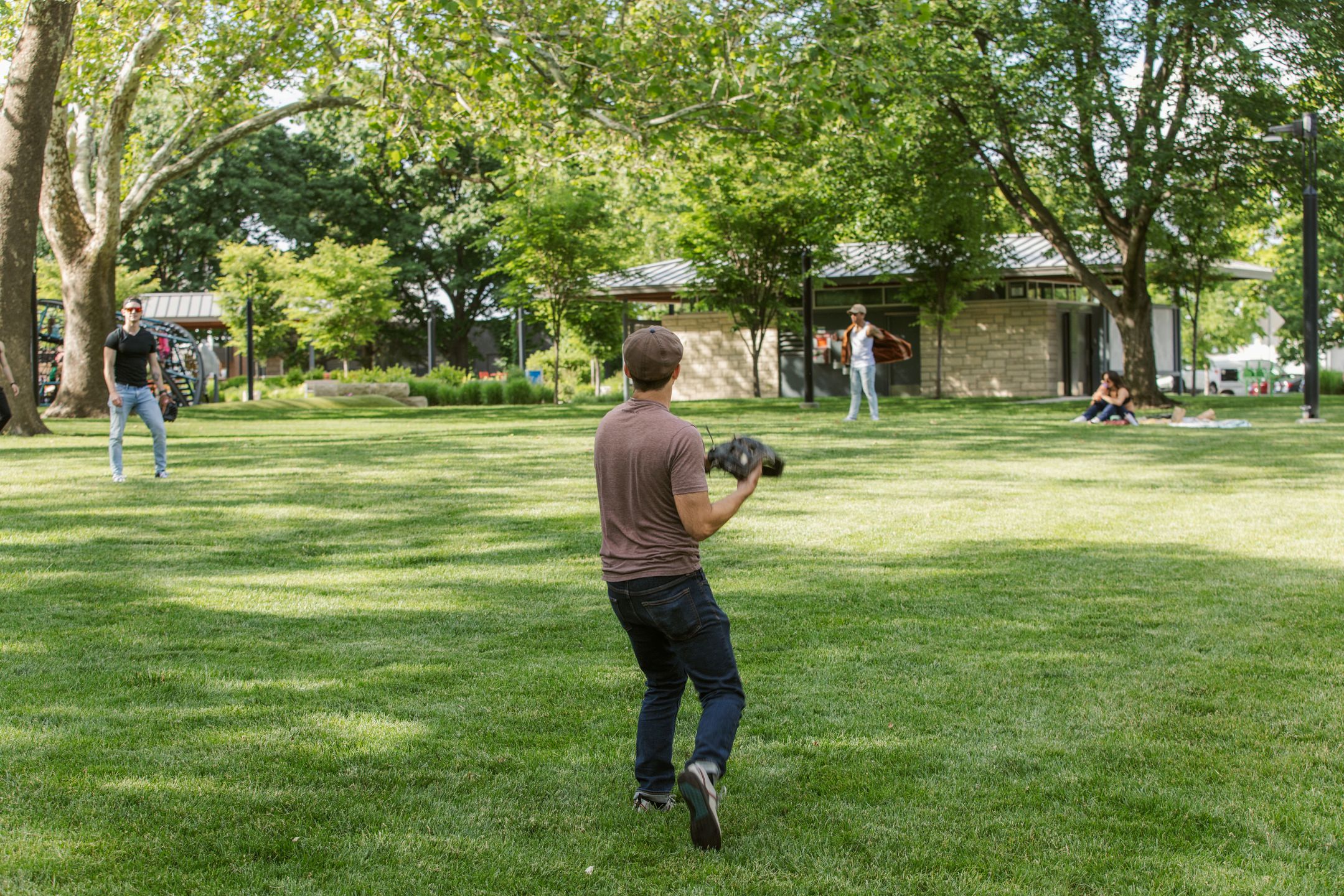 People toss a baseball around in a leafy, green park.
