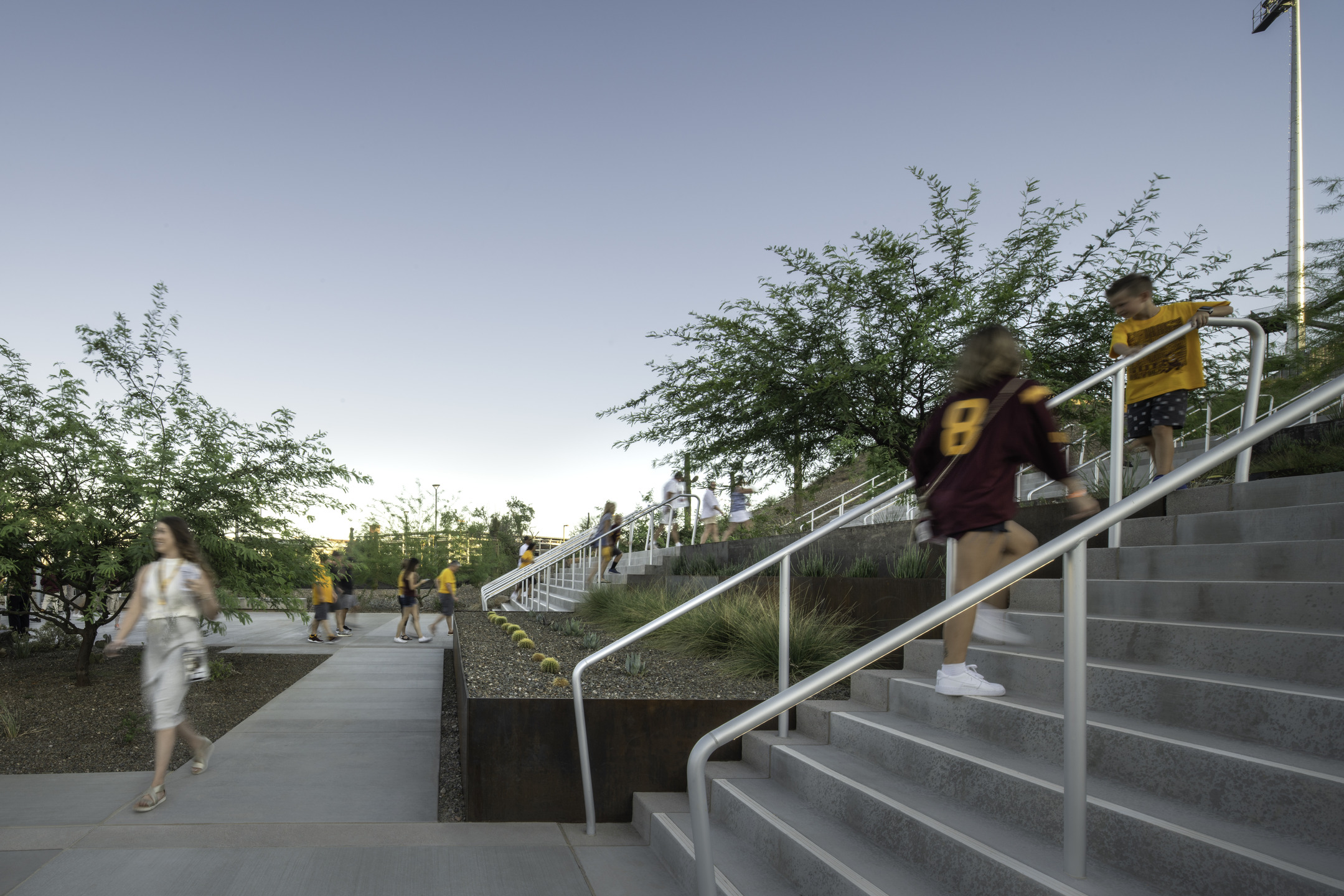 Visitors ascend steps towards the stadium, passing through exterior landscaping.