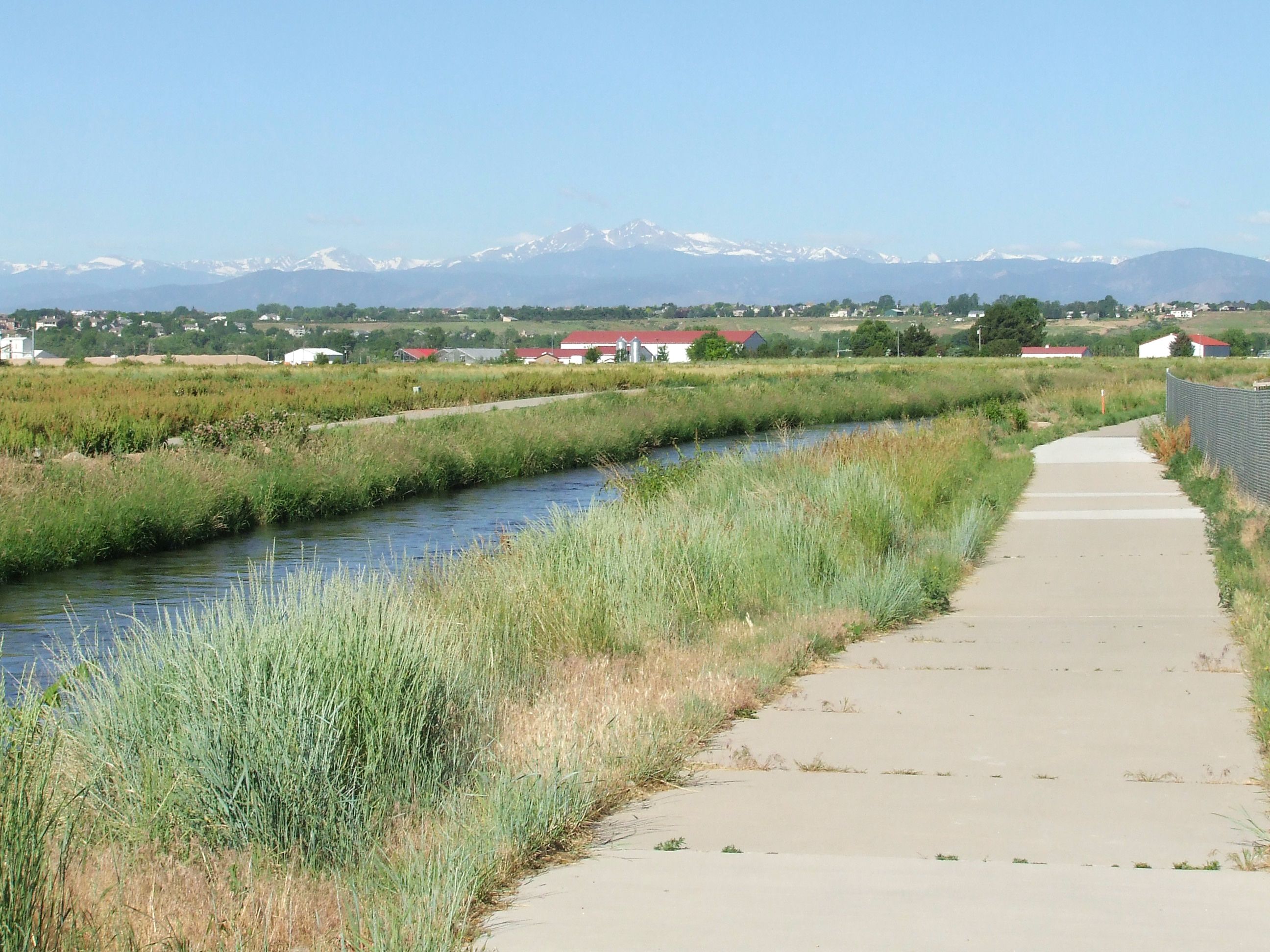 A trail along a creek extends towards a mountain range in the distance.