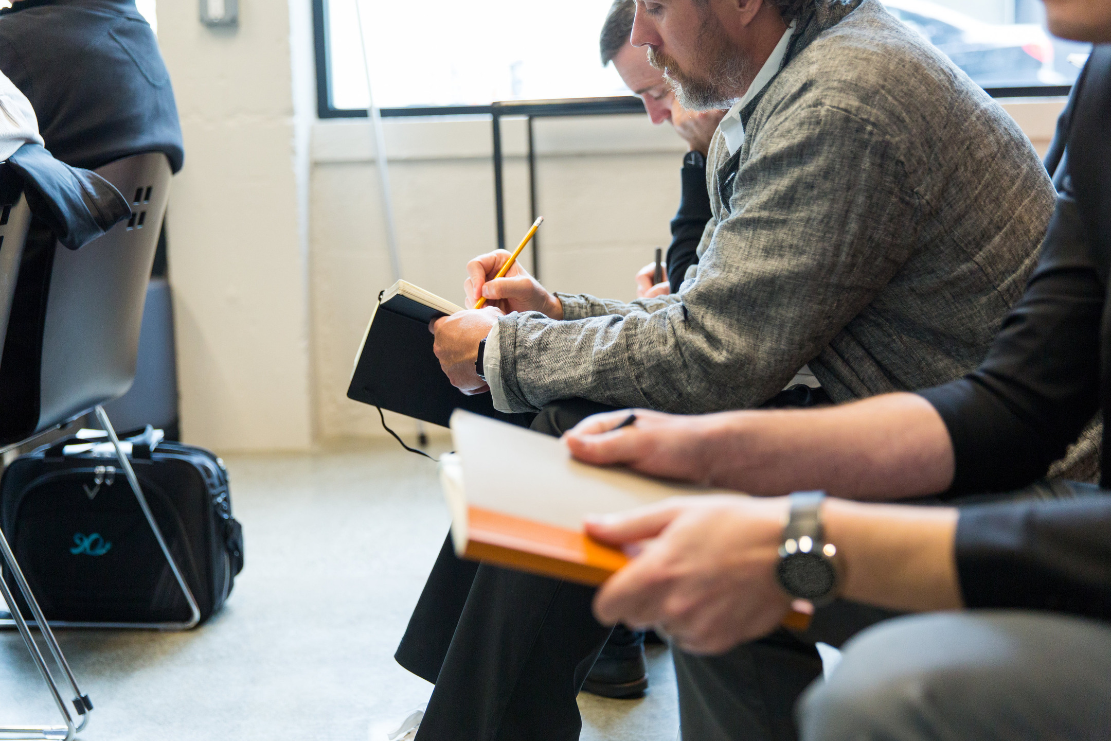 Employees sit in a row of chairs, taking notes in small journals.