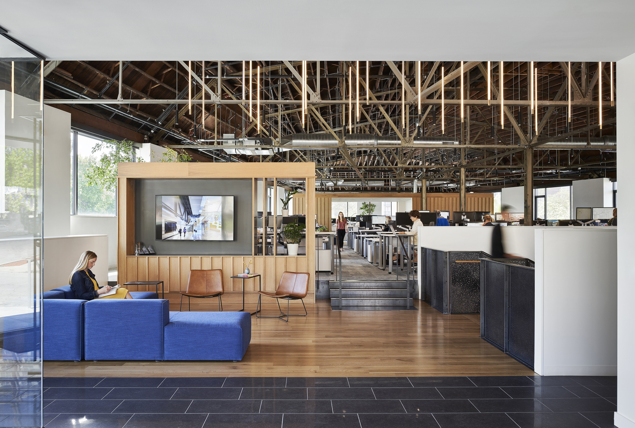 The interior foyer of Multistudio's Kansas City office has a blue couch to the left, dark tile, and light wood flooring. The rest of the office is visible in an open concept layout.