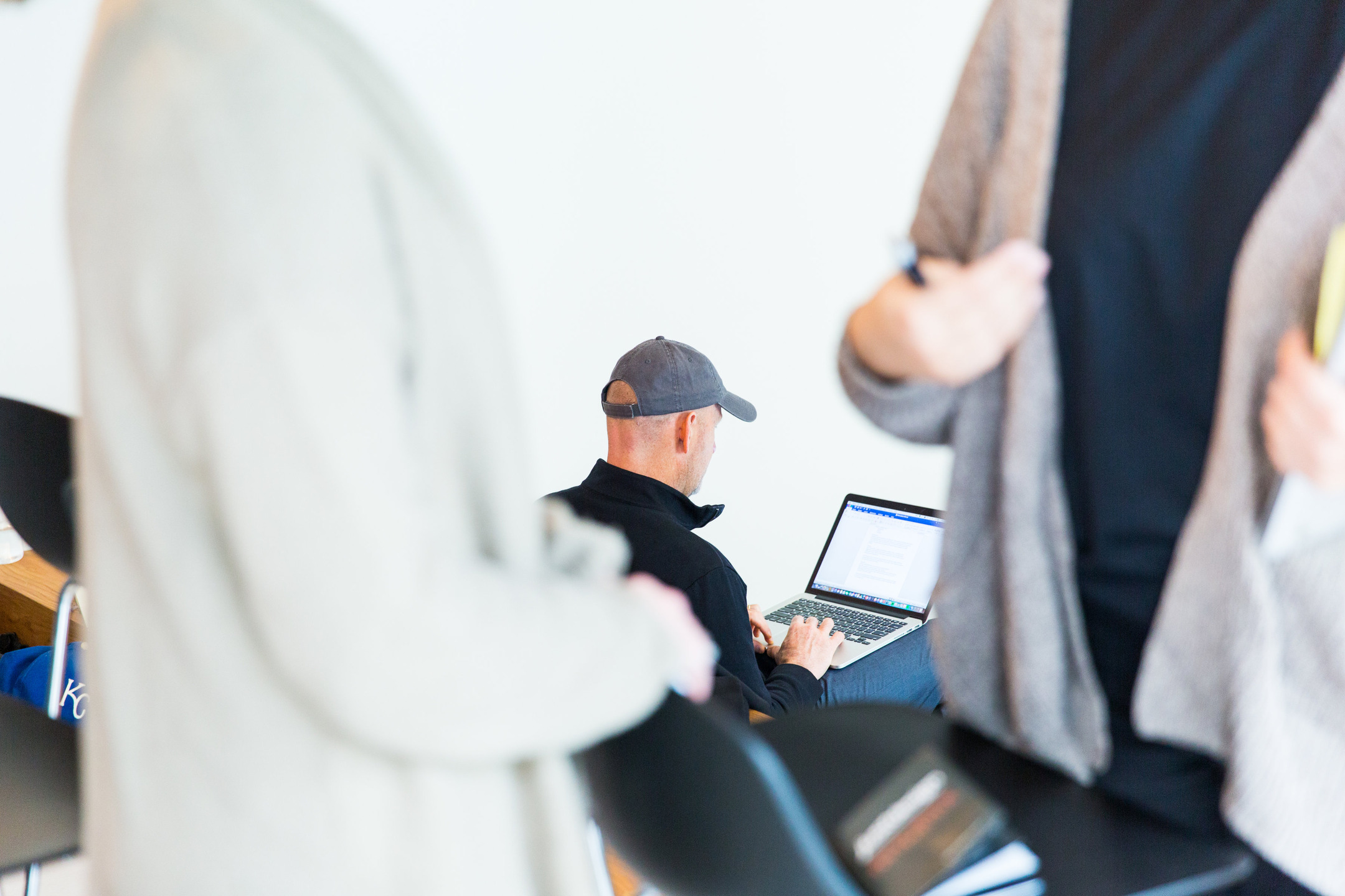 An employee works on a laptop as colleagues converse around him.