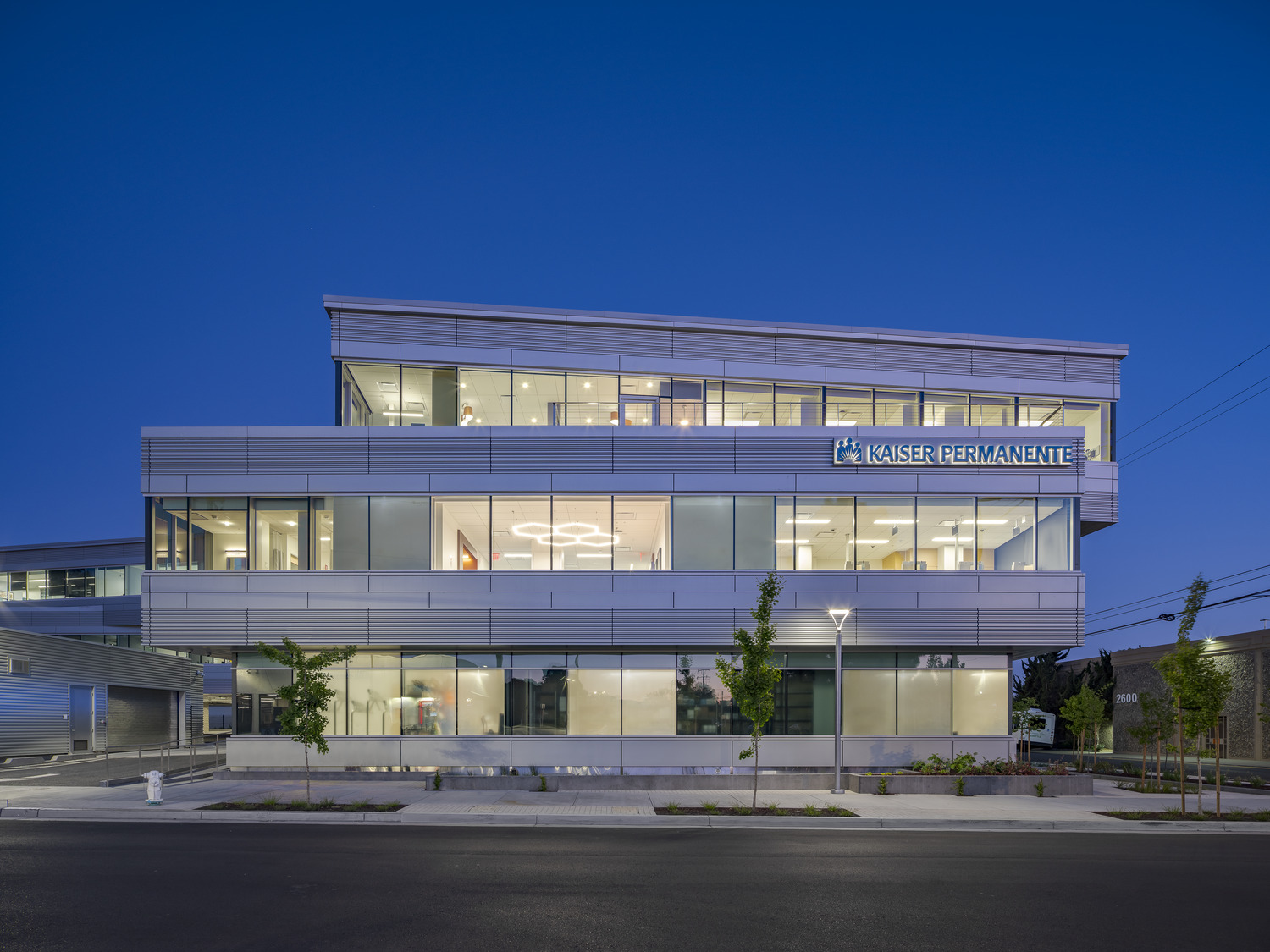 View of the Kaiser Permanente Medical Offices from Parker Street with bicyclists riding by and two people on the rooftop terrace.