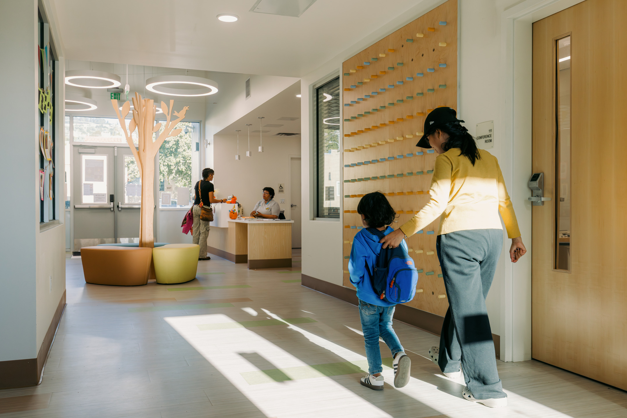 A student and parent walk towards the front desk, situated next to a large wooden cut-out of a tree.