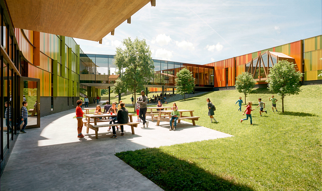 A render shows a courtyard between two school buildings with gradient green, orange, and yellow exterior walls.
