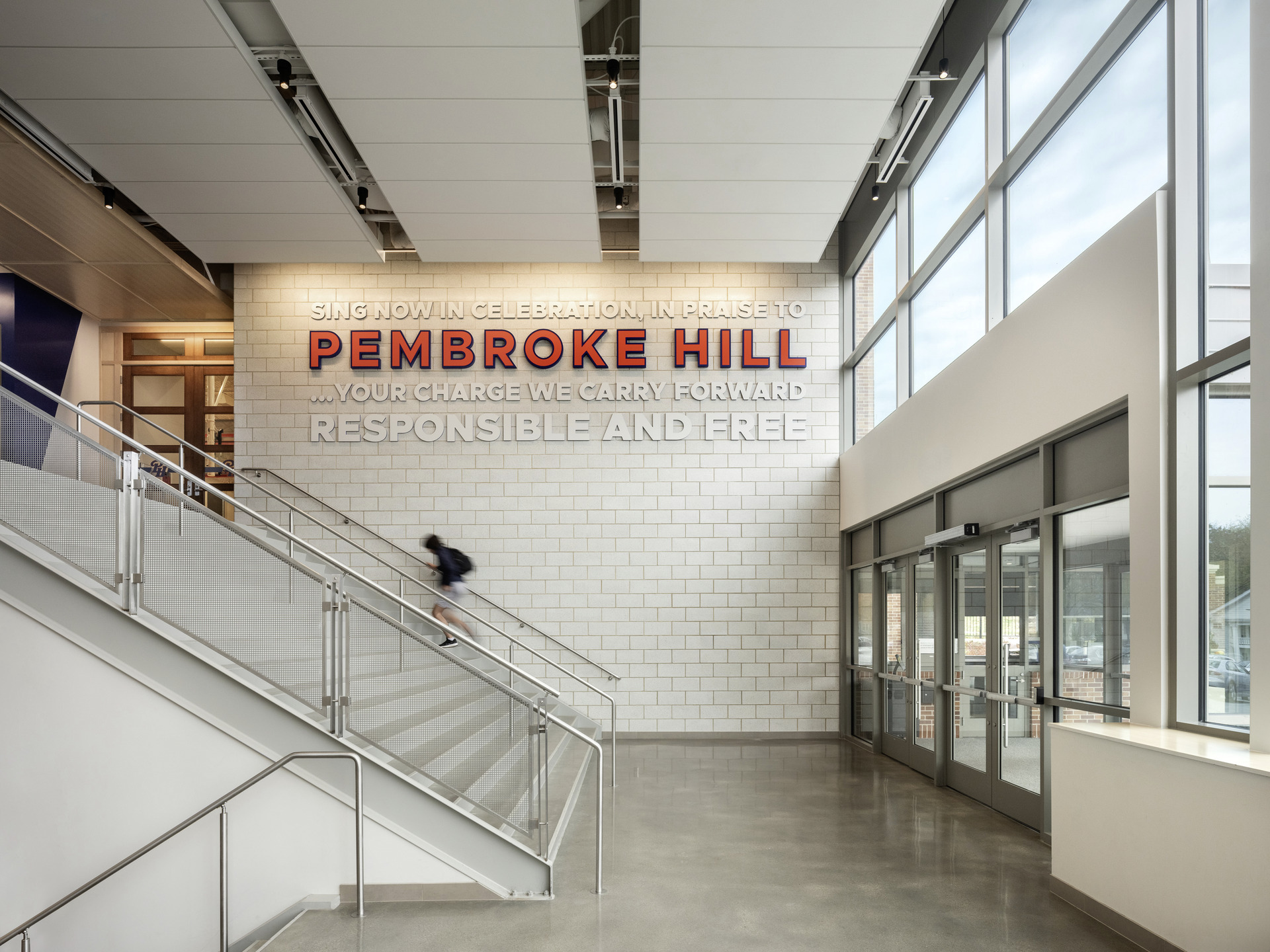 Photo of interior entry of the Bellis Athletics Center with graphic signage that says "Sing now in celebration, in praise to Pembroke Hill... your charge we carry forward responsible and free."