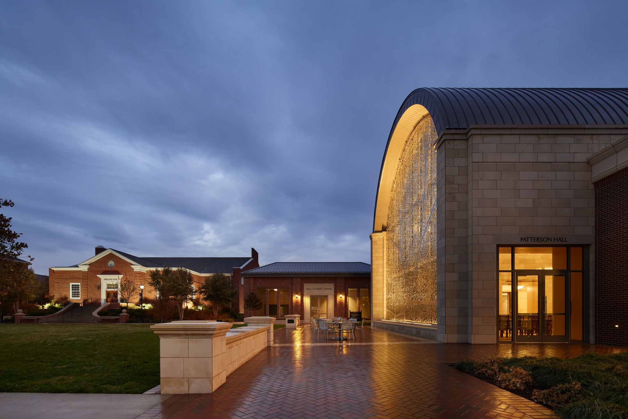 Dusk photo of the campus green with Patterson Hall lit up and the light reflecting off its terrace.
