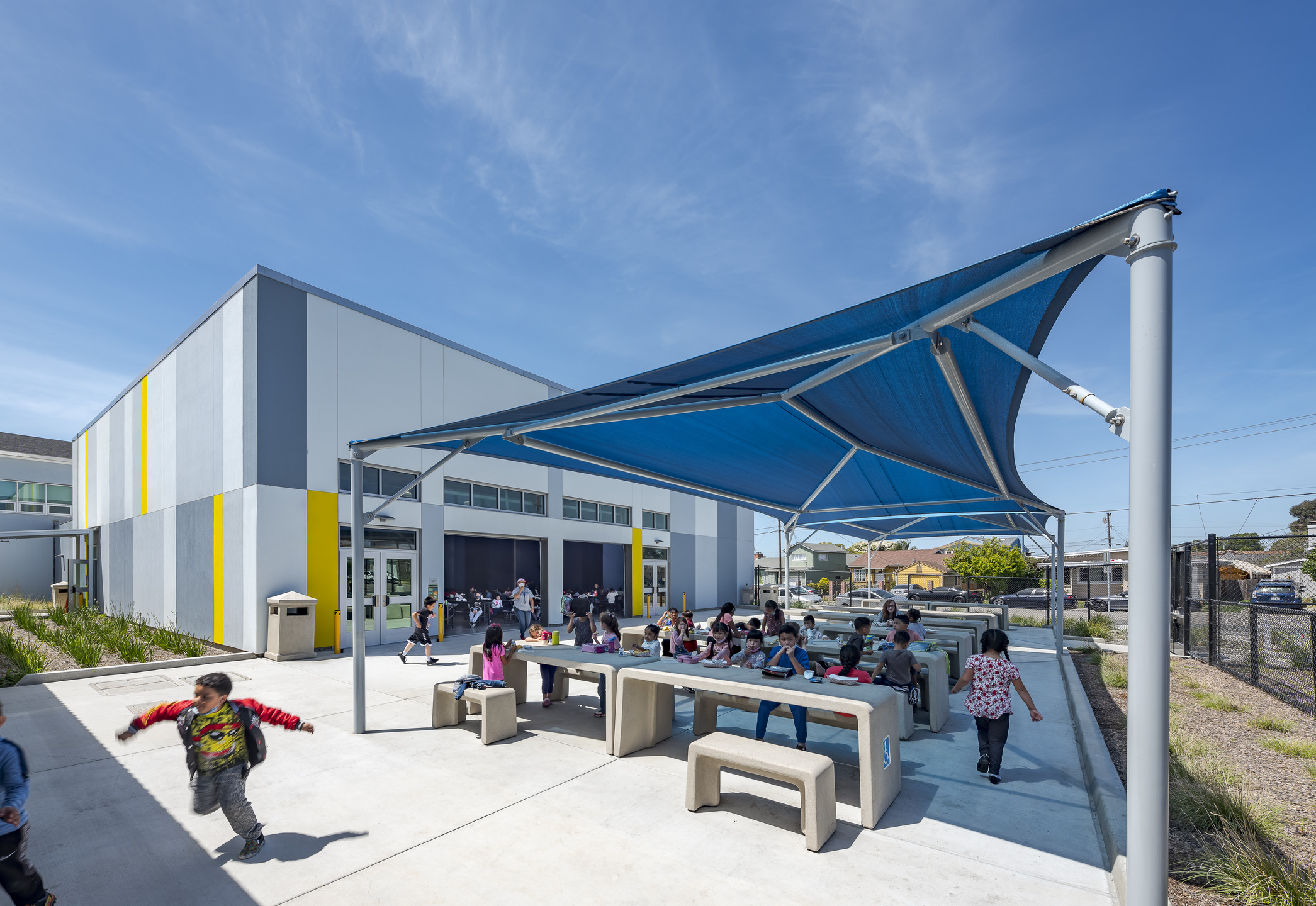 Students sitting at tables under a canopy next to multipurpose room.