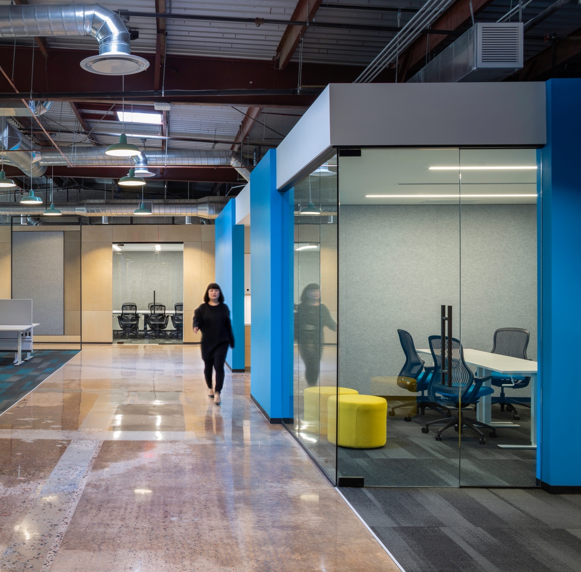 Person walking down workplace hallway adjacent to conference room.