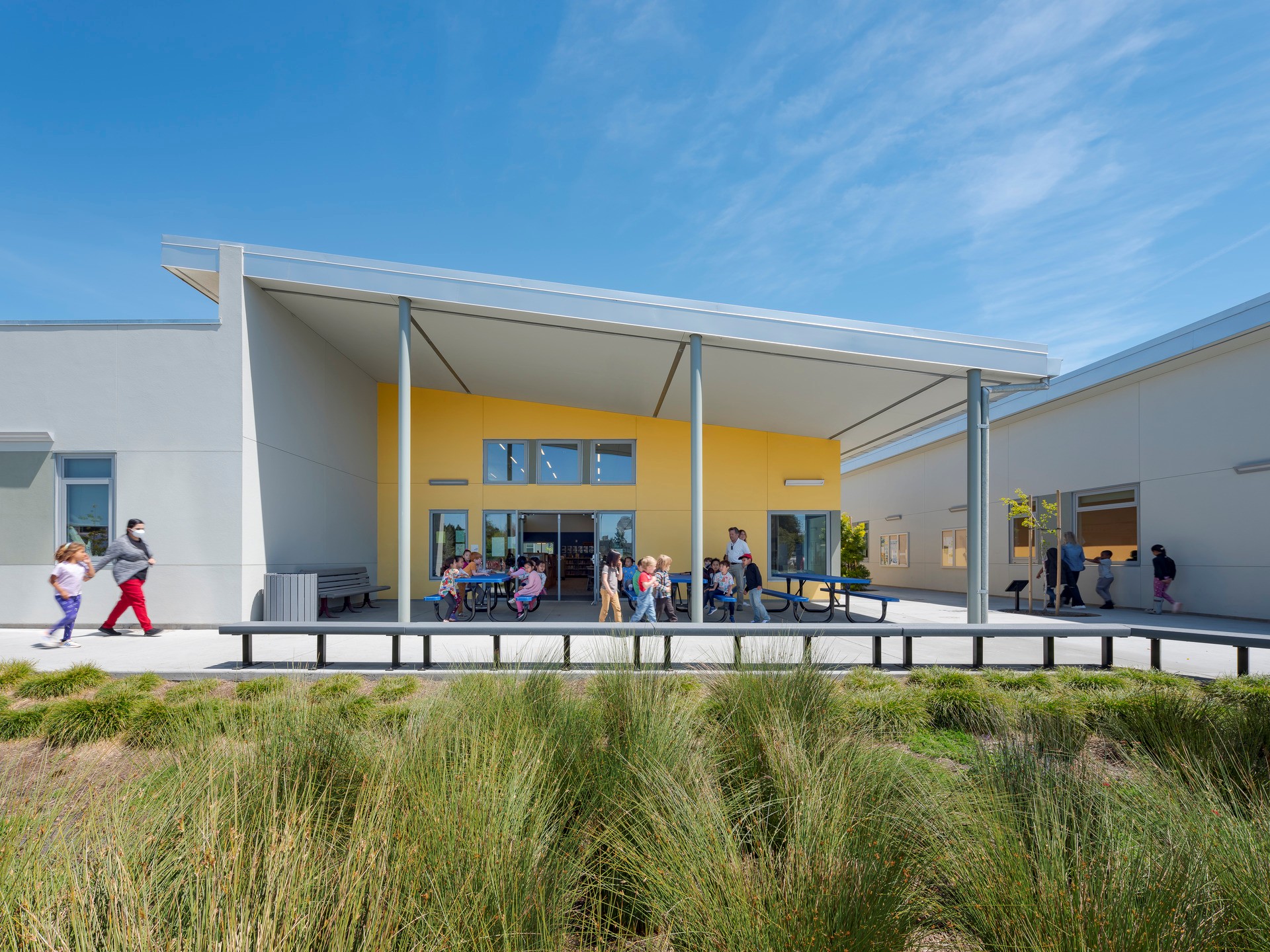 Back entrance of a school library with students sitting at picnic tables.