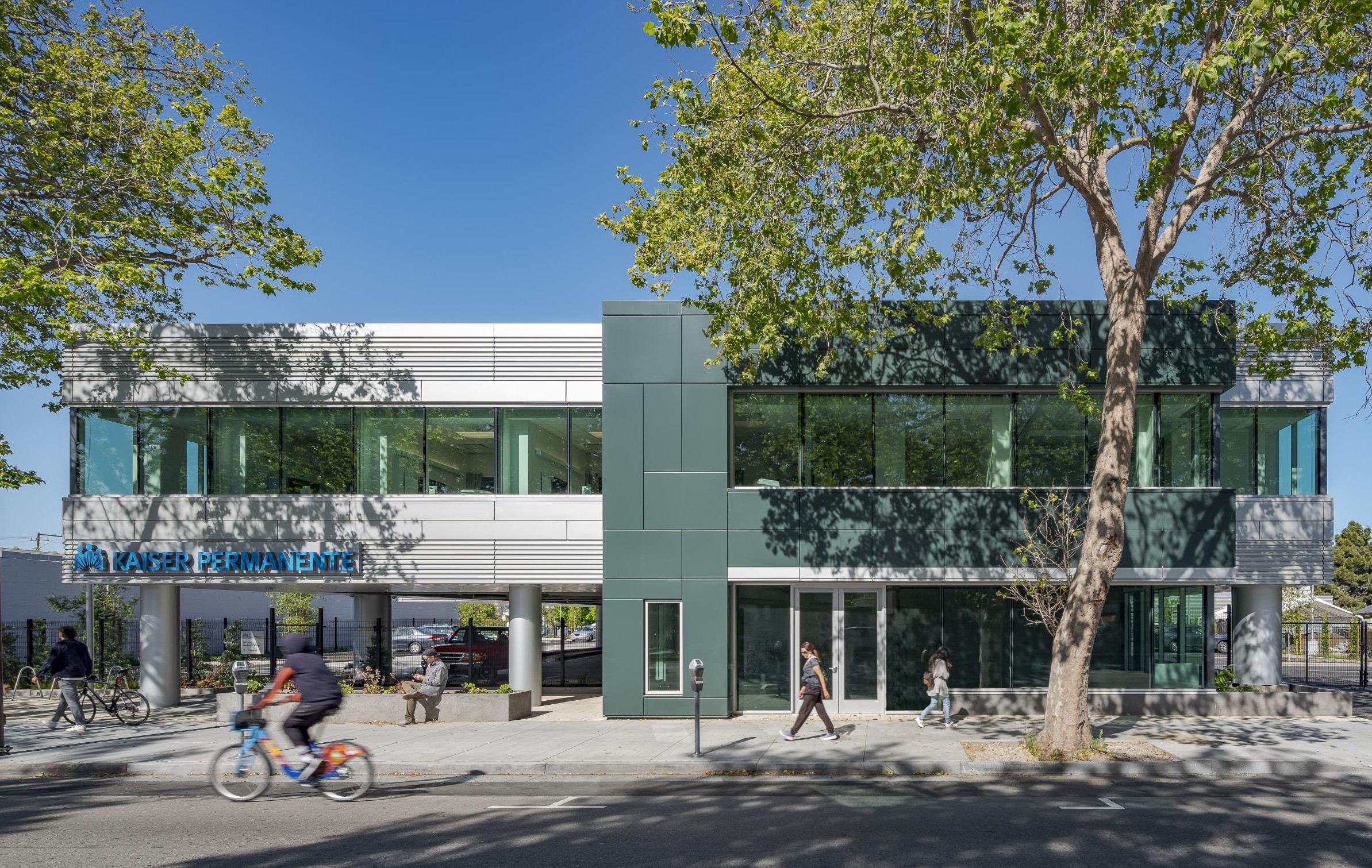 View of the Kaiser Permanente Medical Offices from Parker Street with bicyclists riding by and two people on the rooftop terrace.