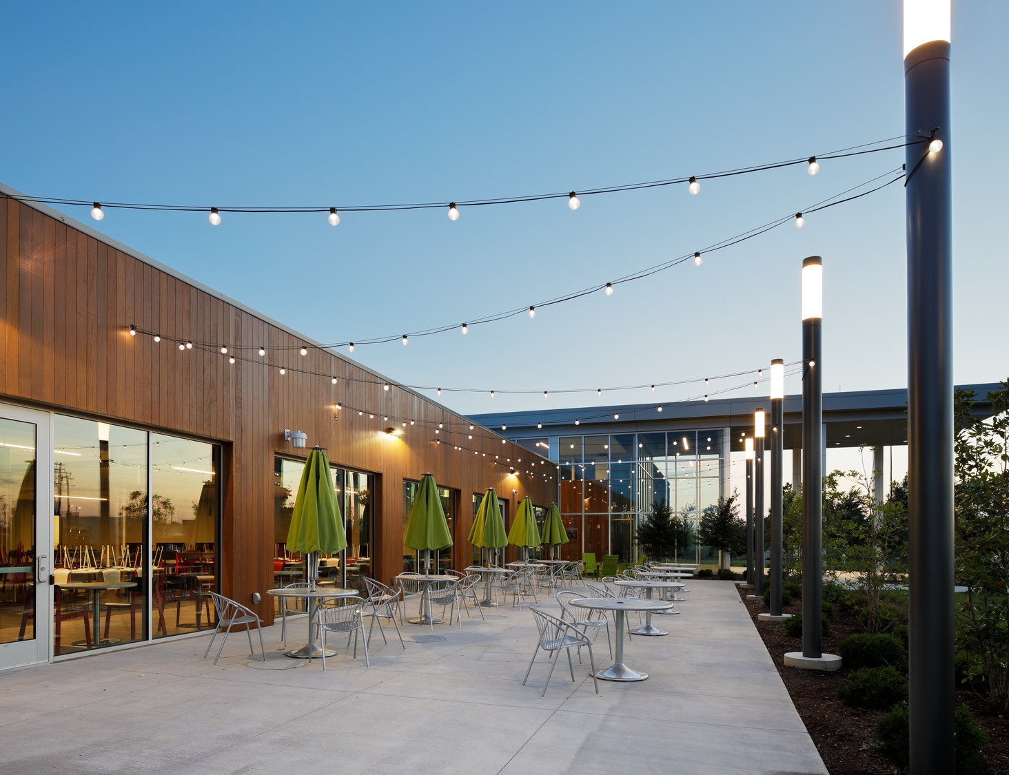 An outdoor patio at KCU features string patio lights and tables with umbrellas. 