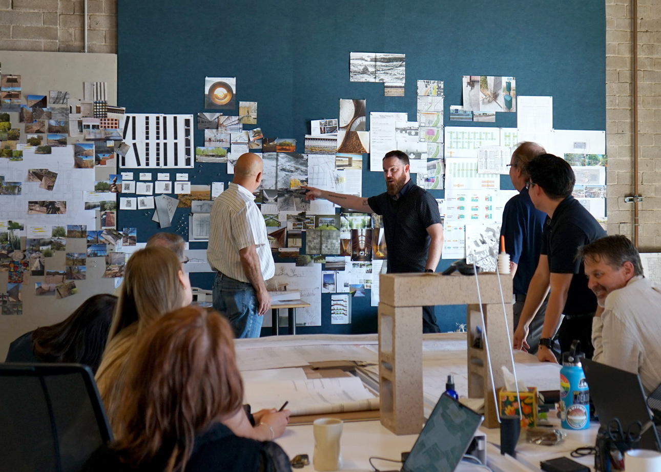 Joey shows partners a project wall that displays dozens of images, drawings, and site photos for a project in Phoenix.
