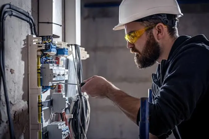 Elektricien met helm en veiligheidsbril werkt aan een zekeringkast