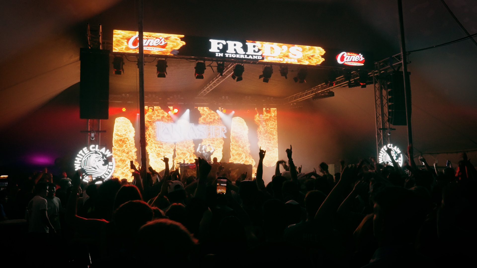 Crowd facing the concert stage at Fred’s in Tigerland, with White Claw branding and orange stage lighting.