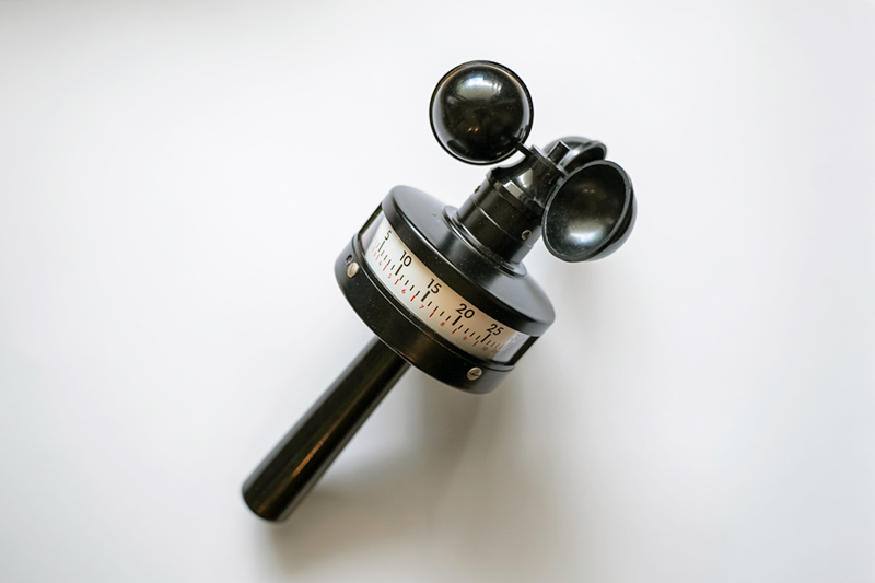 Black handheld anemometer with three cup-shaped sensors and a numeric measurement dial on a white background.